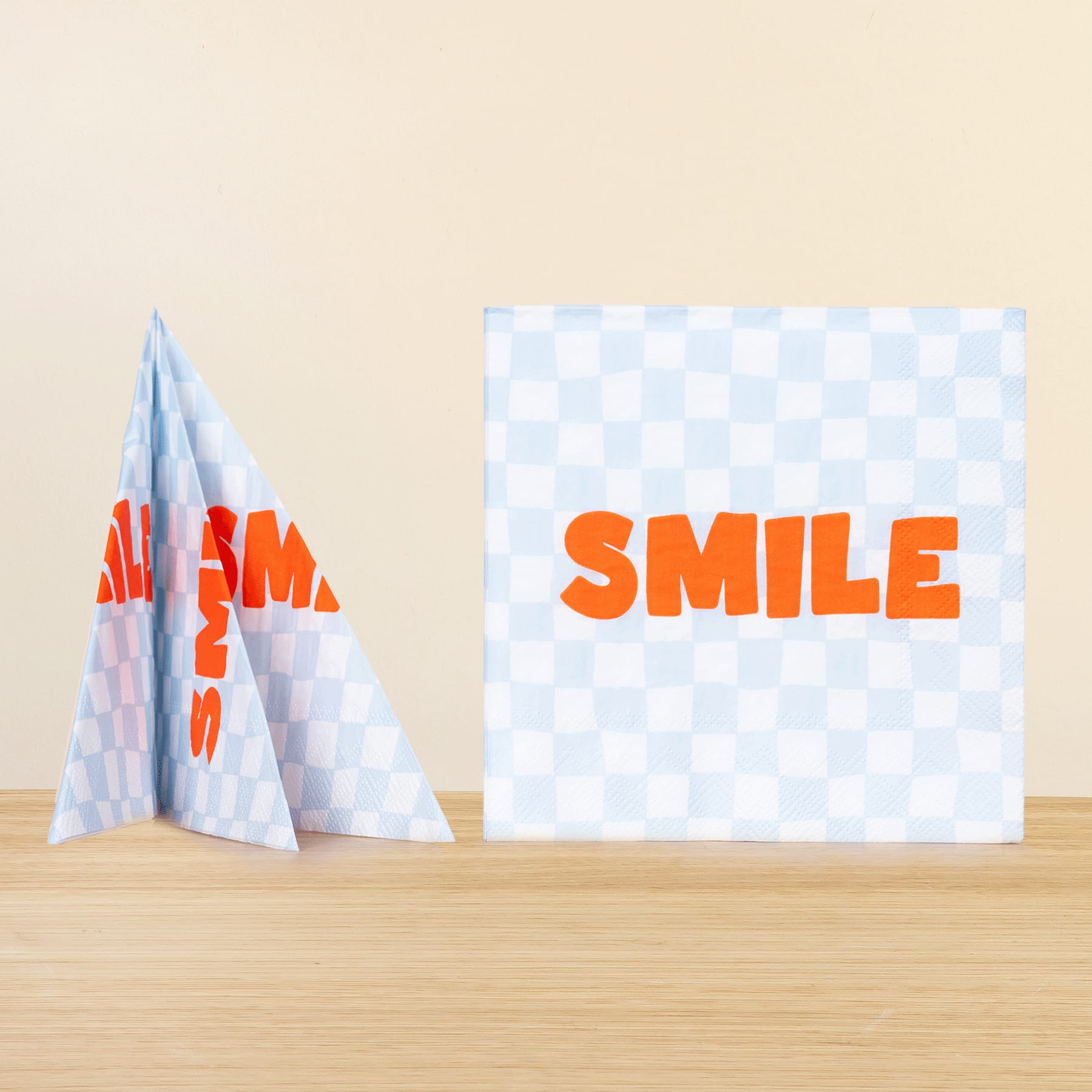 Das Bild zeigt im Vordergrund ein zerknülltes Papierflugzeug, im Hintergrund ist auf einem karierten Hintergrund deutlich das Wort „SMILE“ zu sehen.