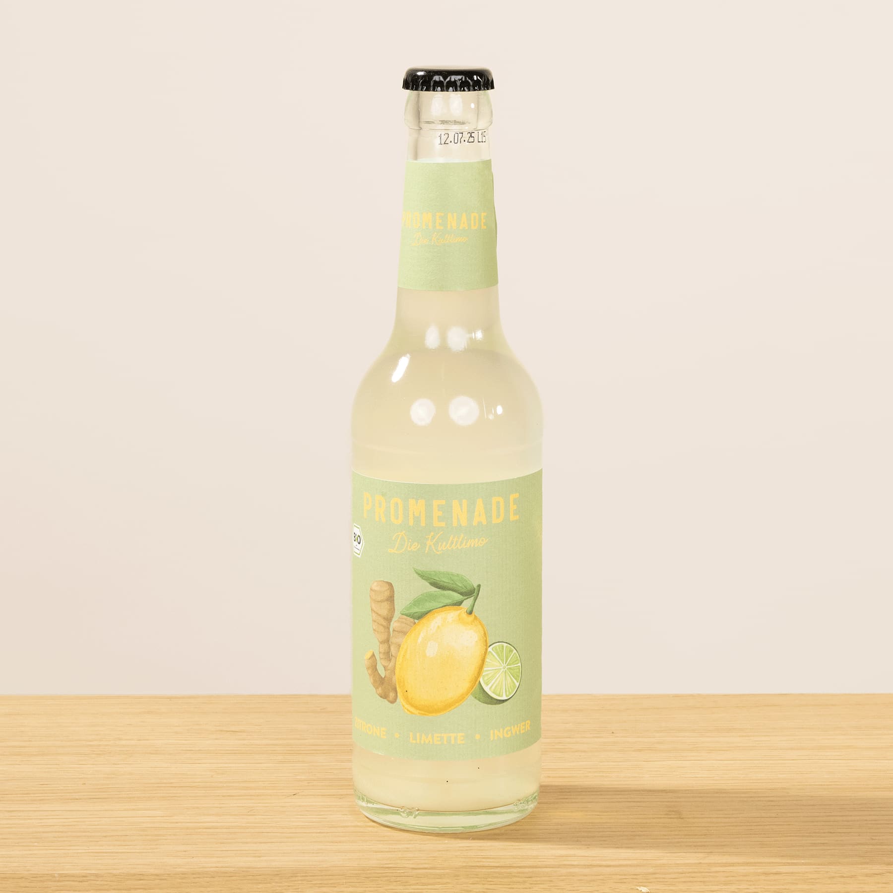 Eine Glasflasche mit selbstgemachter Limonade steht auf einer Holzoberfläche vor einem hellen Hintergrund.