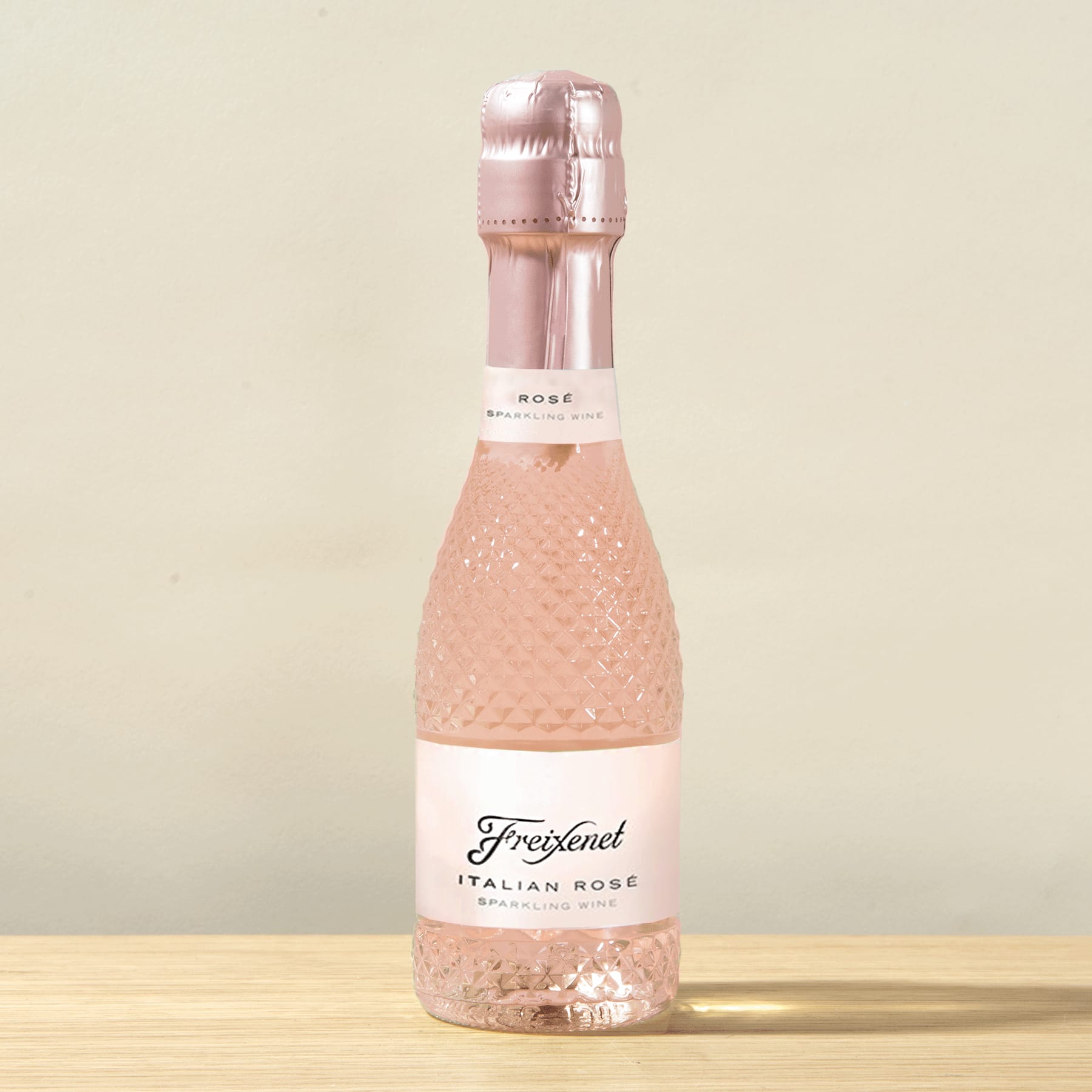 Eine rosafarbene, prickelnde Flasche italienischen Roséweins steht auf einer Holzoberfläche vor einem hellen Hintergrund.