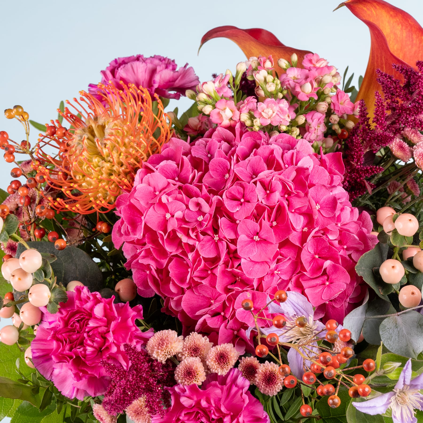 Ein leuchtender Strauß aus rosa Hortensien, orangefarbenen Chrysanthemen und anderen bunten Blumen vor einem klaren blauen Himmel.