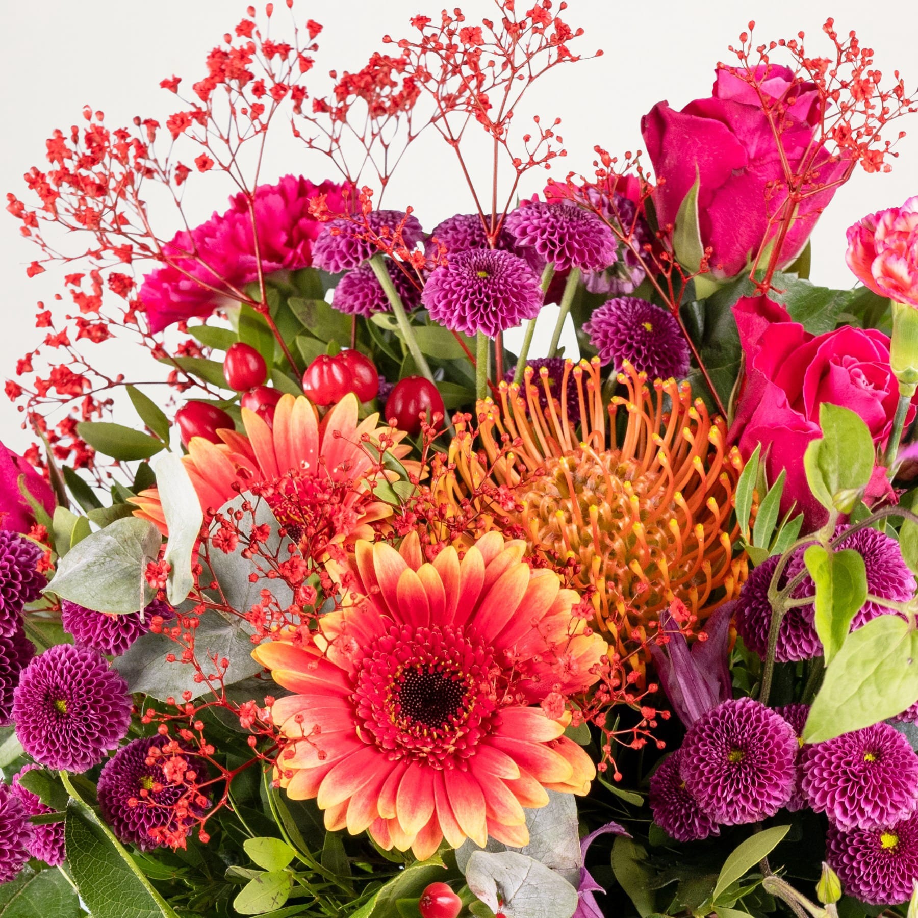 Ein lebendiger Strauß verschiedener roter, rosa und orangefarbener Blumen, darunter Rosen, Gerbera und Chrysanthemen, vor einem schlichten weißen Hintergrund.