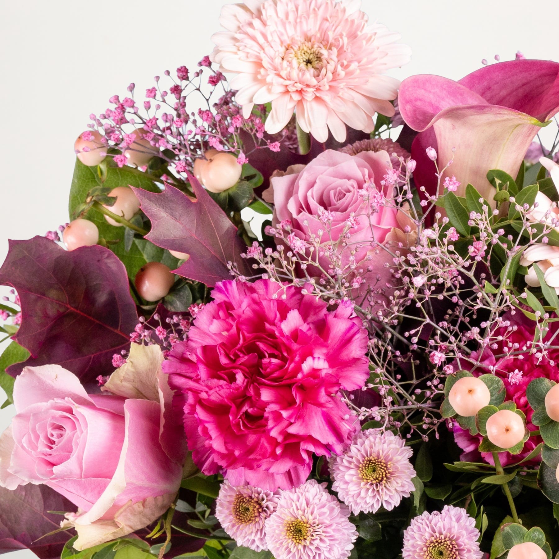 Ein farbenfroher Strauß verschiedener rosa und violetter Blumen, darunter Rosen, Nelken und Chrysanthemen, arrangiert vor einem schlichten weißen Hintergrund.