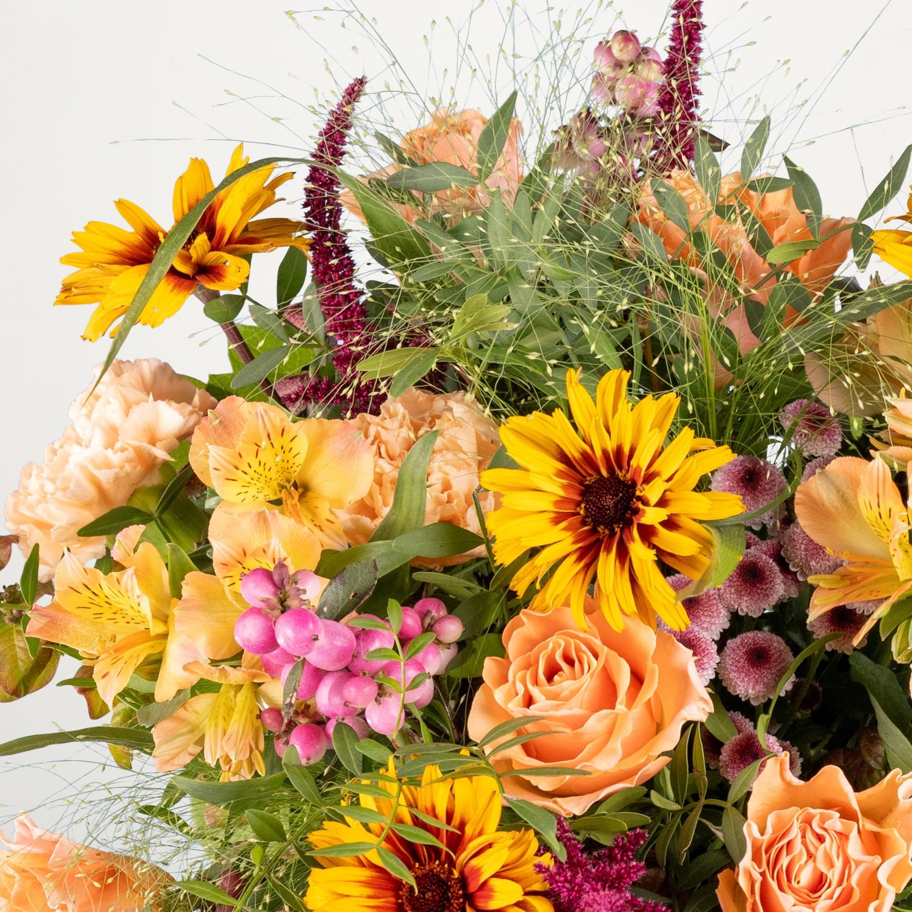Ein lebendiger Strauß bunter Blumen, darunter gelbe Sonnenblumen, orangefarbene Rosen und verschiedene andere Blüten, arrangiert vor einem schlichten weißen Hintergrund.