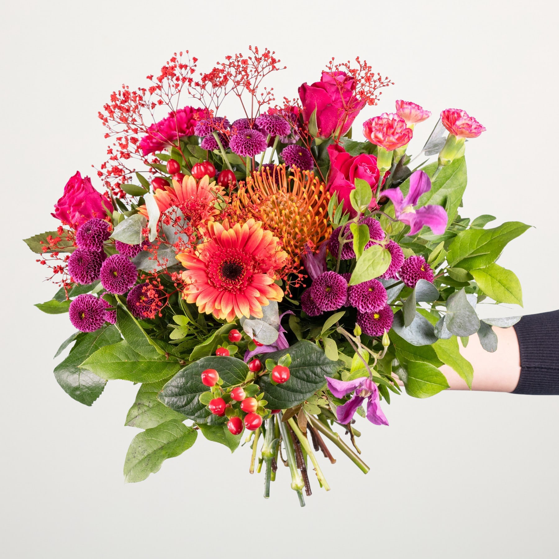 Ein lebendiger Strauß verschiedener bunter Blumen, darunter rote Rosen, rosa Gerbera und lila Chrysanthemen, arrangiert vor einem schlichten weißen Hintergrund.
