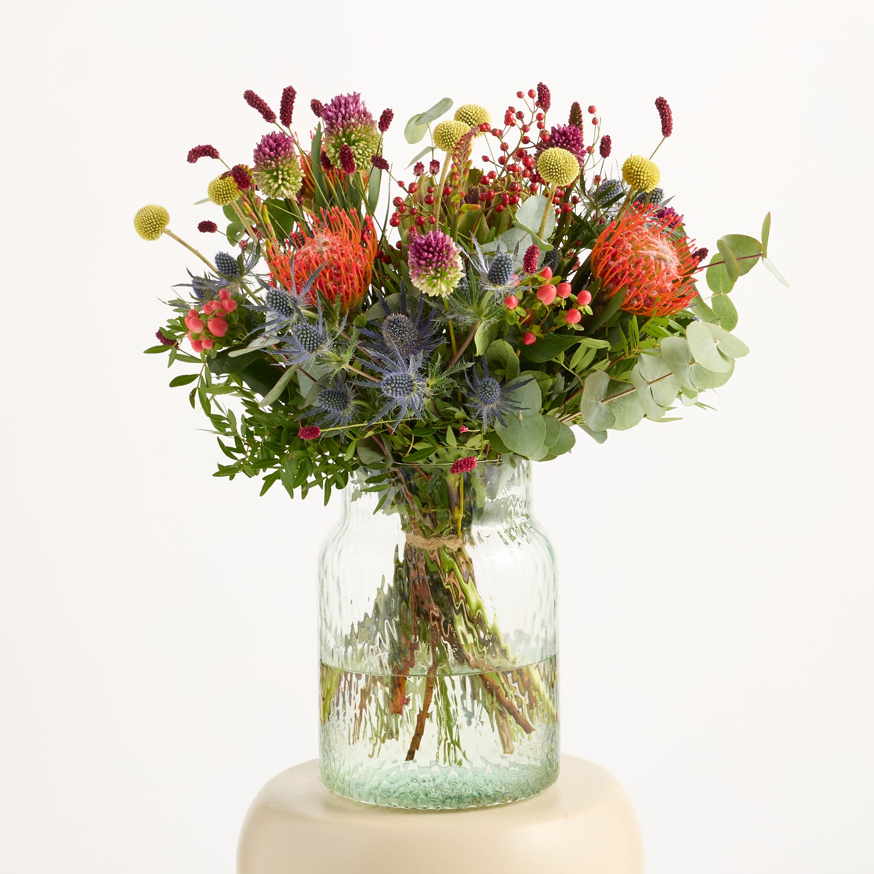 Ein lebendiger und farbenfroher Strauß verschiedener Blumen, darunter Chrysanthemen, Dahlien und andere herbstlich inspirierte Blüten, in einem rustikalen, natürlichen Stil vor einem schlichten weißen Hintergrund arrangiert.