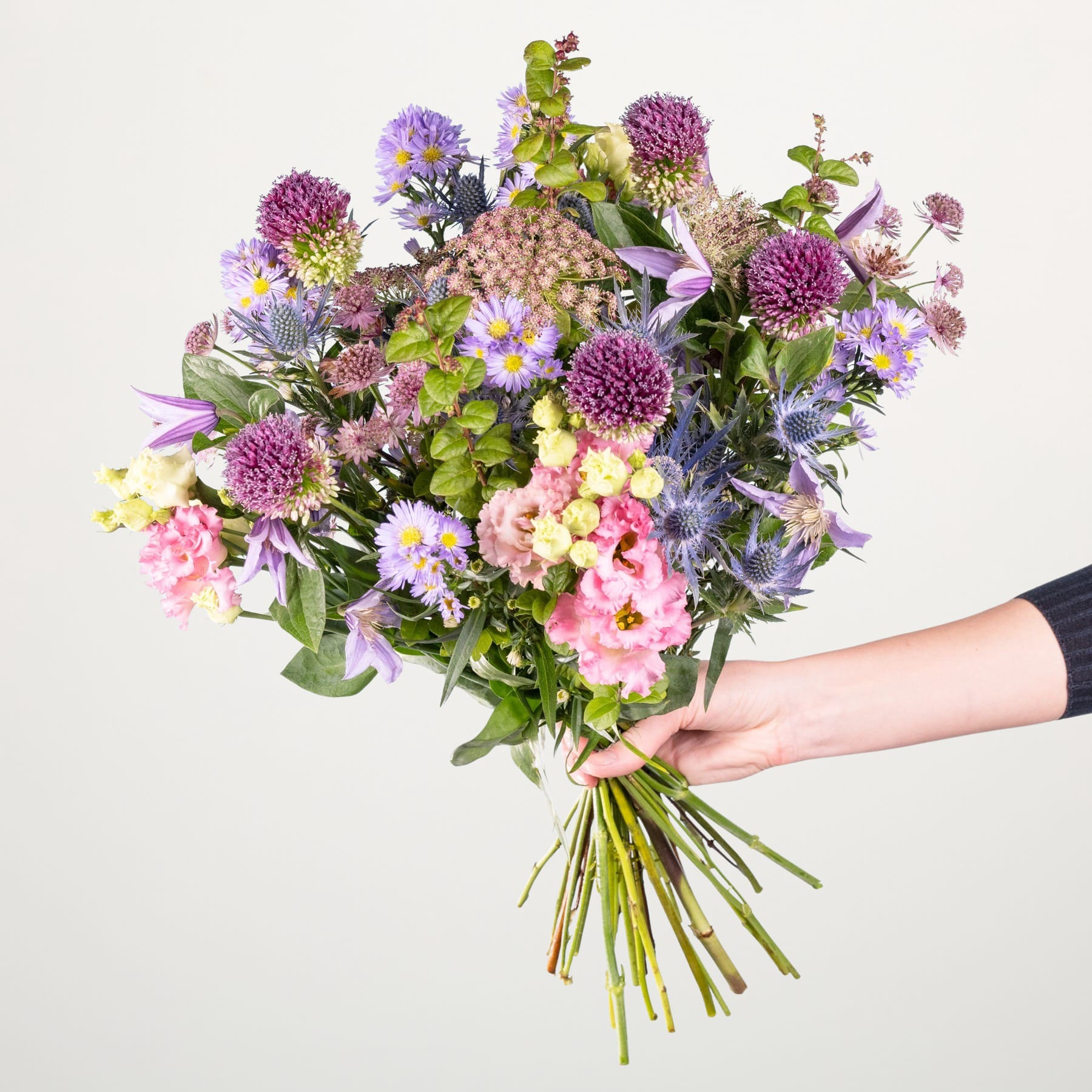 Ein leuchtender Strauß verschiedener bunter Blumen, darunter Chrysanthemen, Gänseblümchen und andere Blüten, den eine Person vor einem schlichten weißen Hintergrund in den Händen hält.
