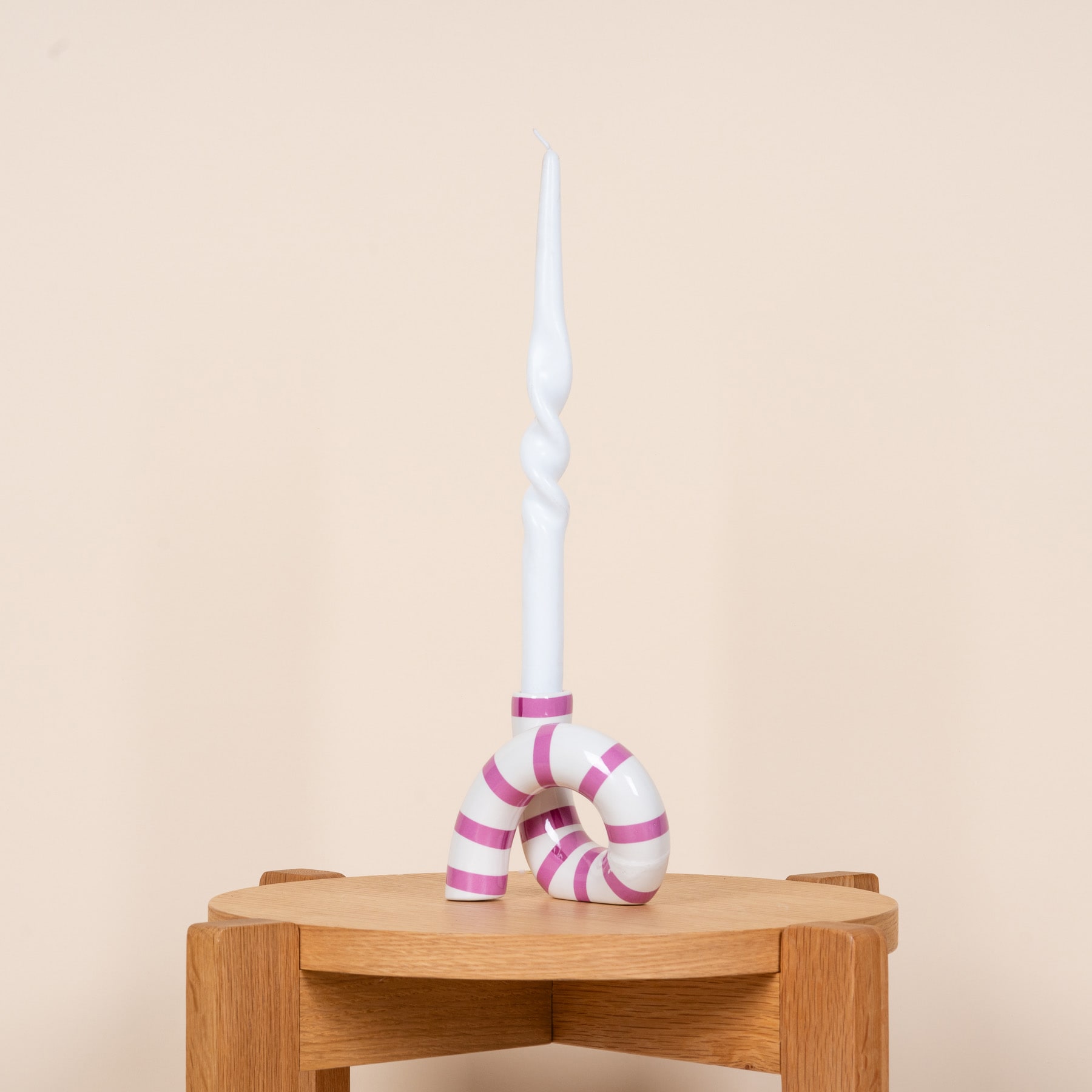 Auf einem Holztisch steht eine weiße Spiralkerze, daneben ist vor einem beigen Hintergrund ein rosa-weiß gestreiftes Ornament platziert.