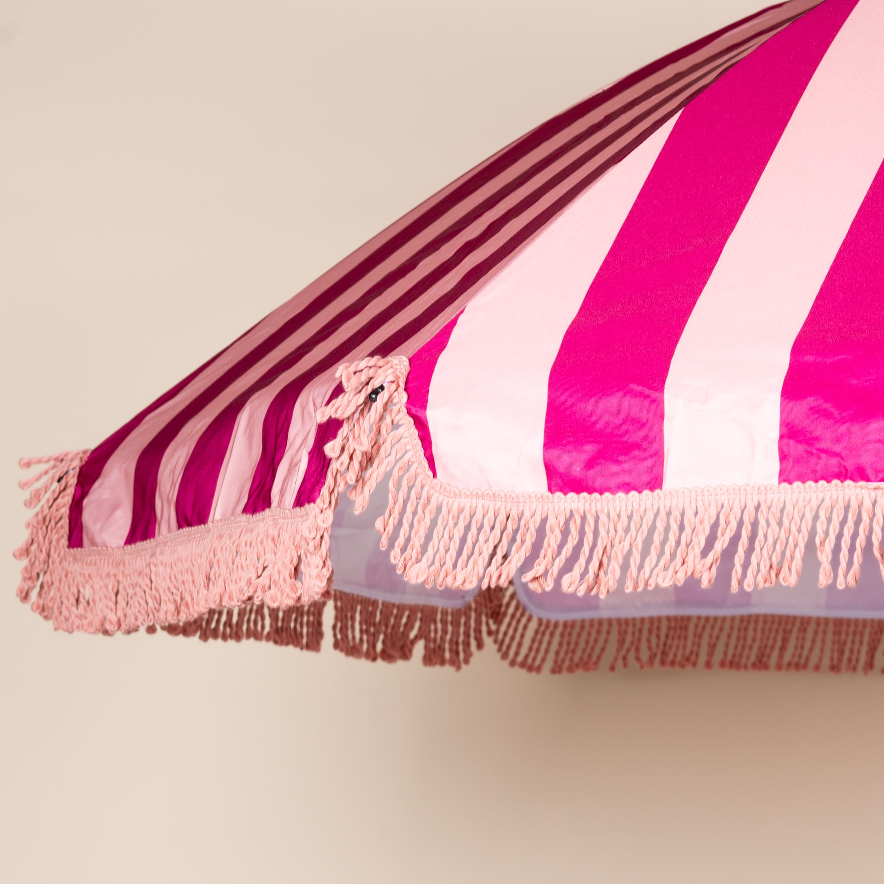 Ein leuchtend rosa-weiß gestreifter Baldachin mit Fransenquasten, der vor einem neutralen Hintergrund aufgehängt ist.