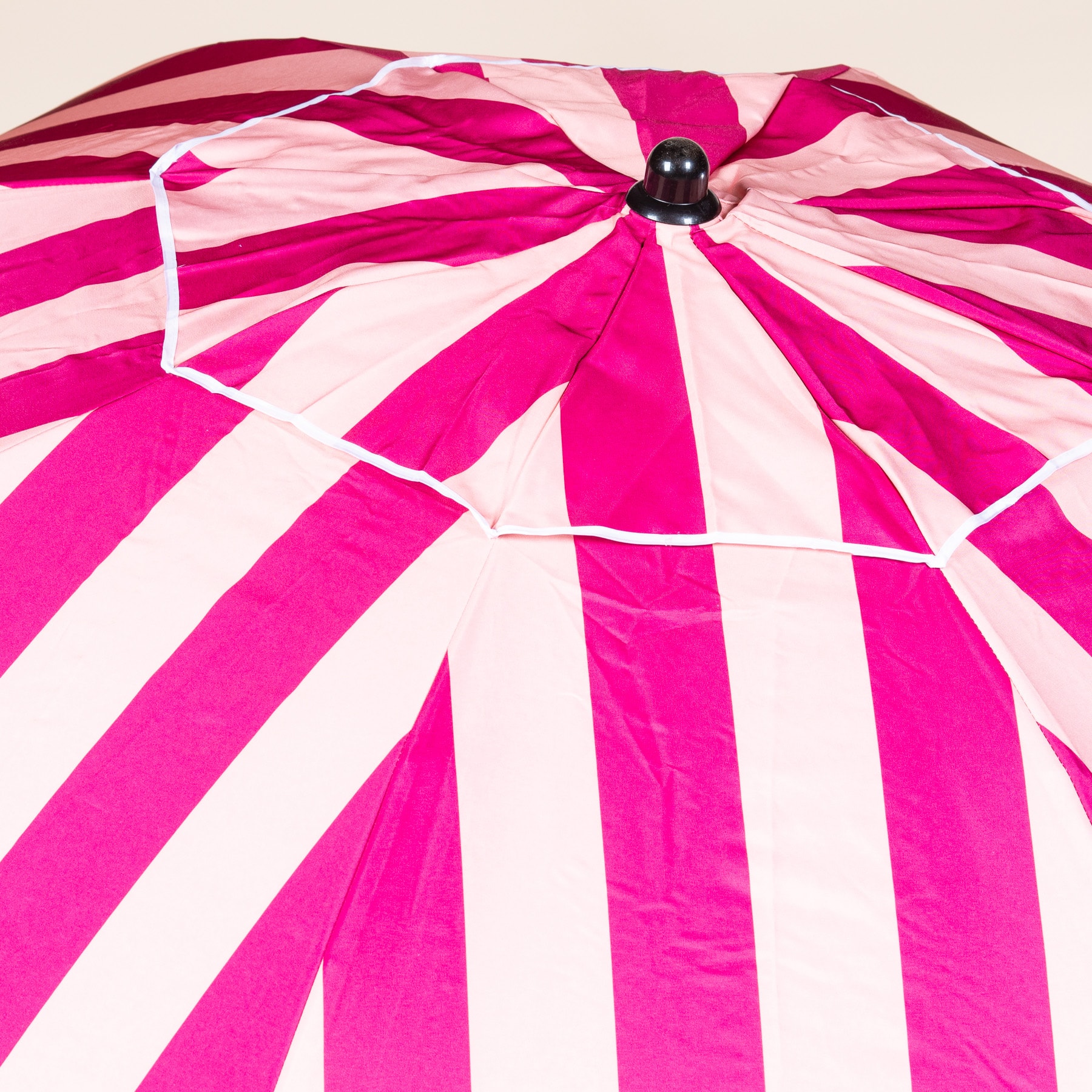 Ein leuchtend rosa-weiß gestreifter Regenschirm mit schwarzem Griff und Knauf vor einem schlichten Hintergrund.