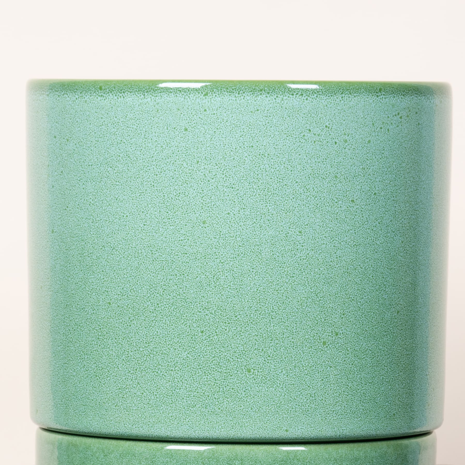 Ein mintgrüner Blumentopf oder Topf aus Keramik mit glatter, matter Oberfläche steht vor einem schlichten weißen Hintergrund.