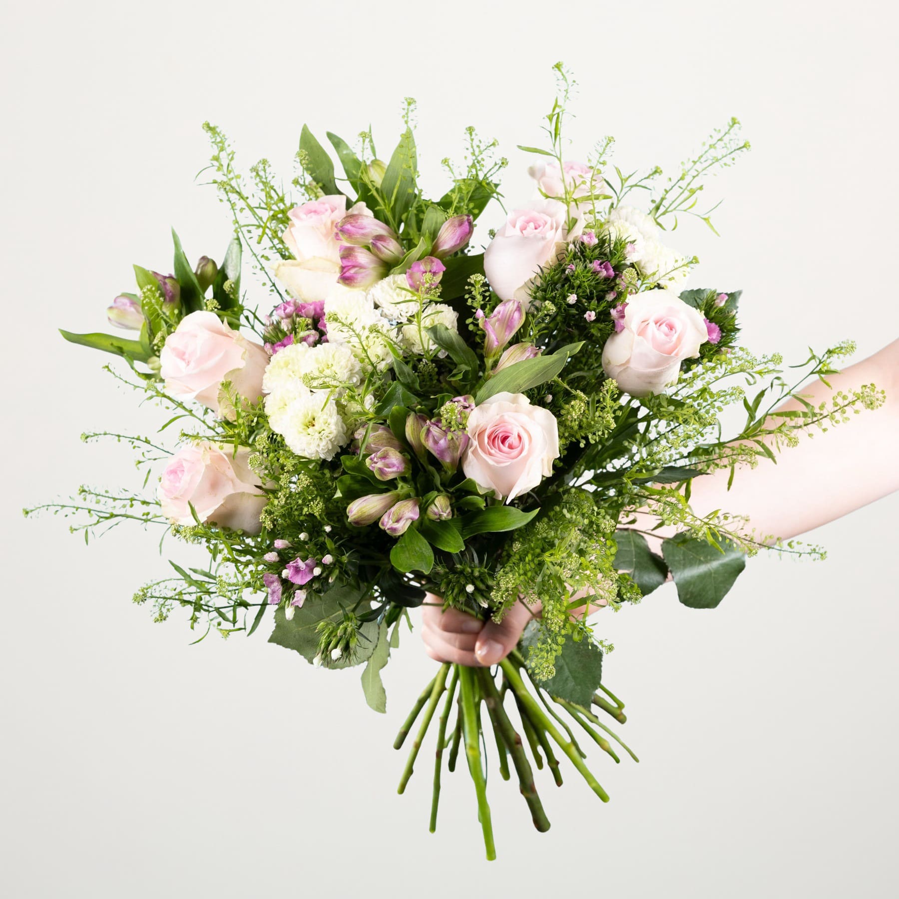Ein lebendiger Strauß rosa und weißer Rosen, Grünpflanzen und anderer zarter Blumen, üppig und natürlich arrangiert vor einem schlichten weißen Hintergrund.