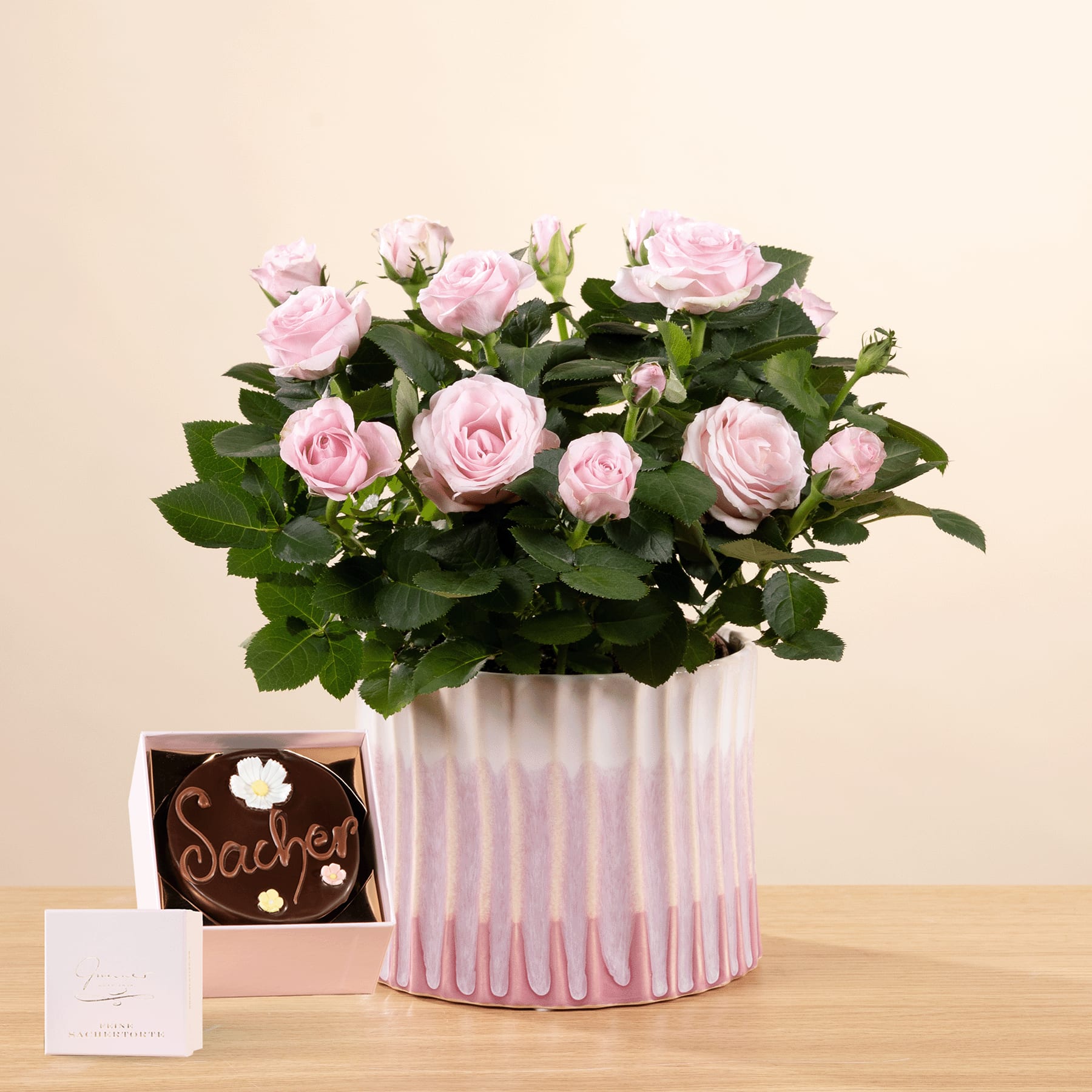 Ein Strauß zartrosa Rosen steht in einer dekorativen Vase auf einem Holztisch, begleitet von einem kleinen gerahmten Gegenstand und einer handgeschriebenen Notiz.
