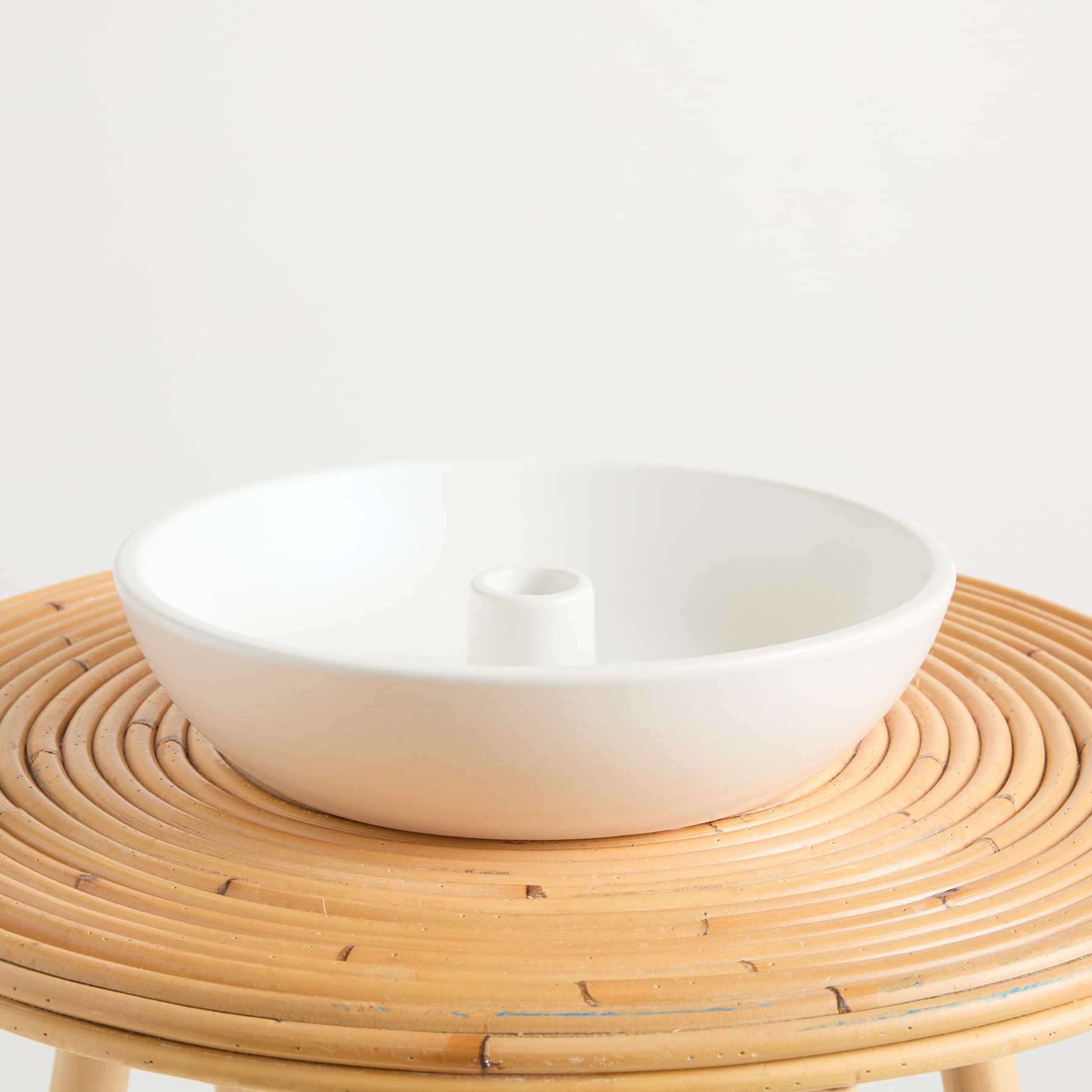 Eine weiße Keramikschüssel steht auf einer runden Bambusplatte vor einem schlichten weißen Hintergrund.