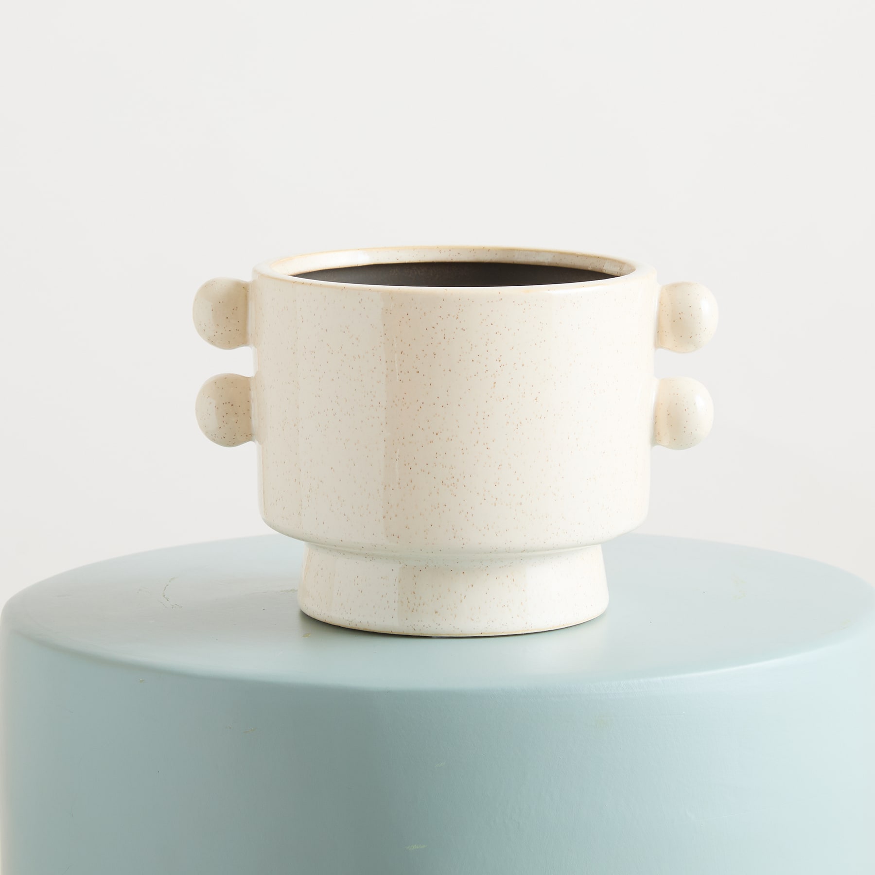 Ein weißer Keramikbecher oder eine Tasse steht auf einer hellblauen runden Plattform vor einem schlichten weißen Hintergrund.