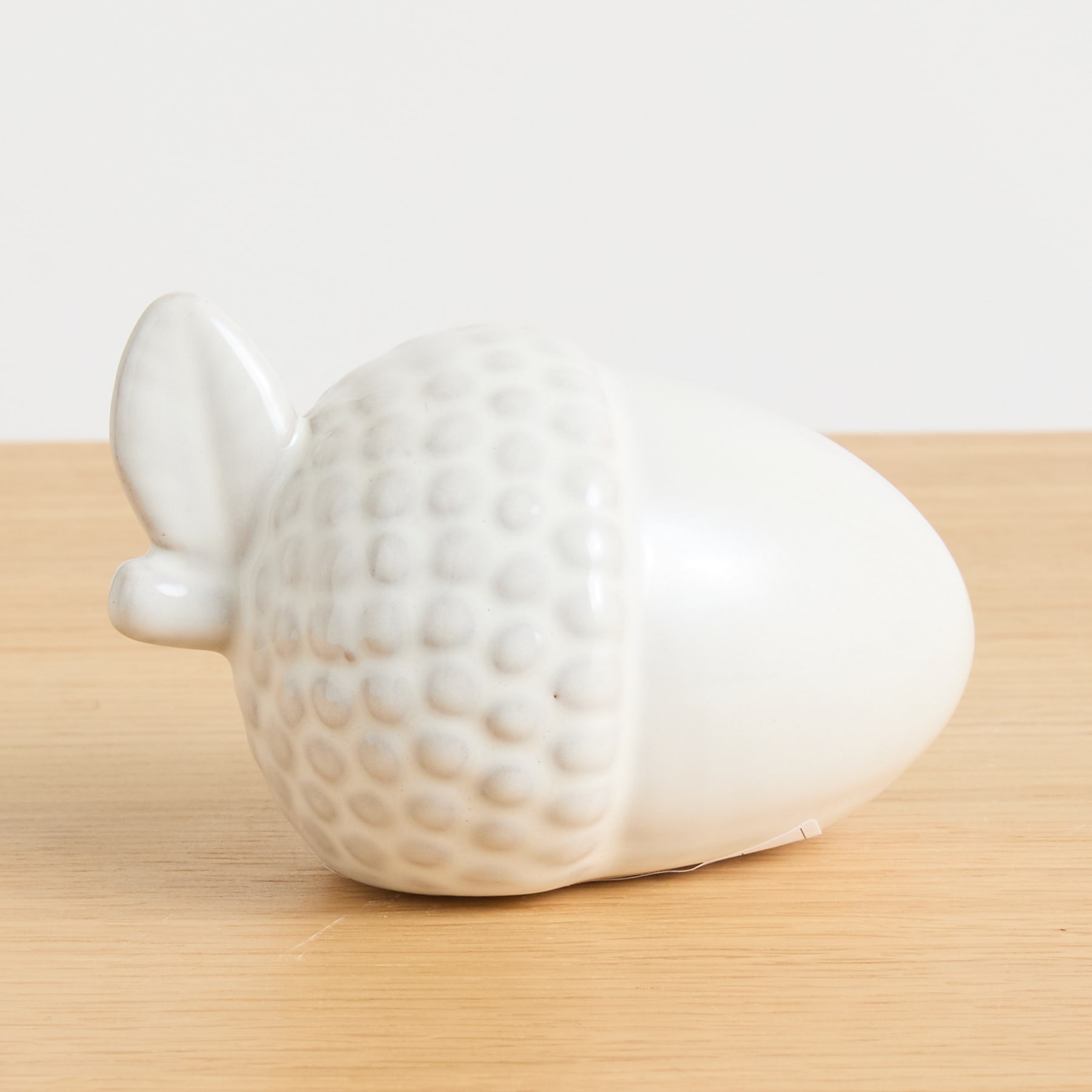 Eine weiße Keramikfigur eines Vogels oder vogelähnlichen Wesens liegt auf einer Holzoberfläche vor einem schlichten Hintergrund.