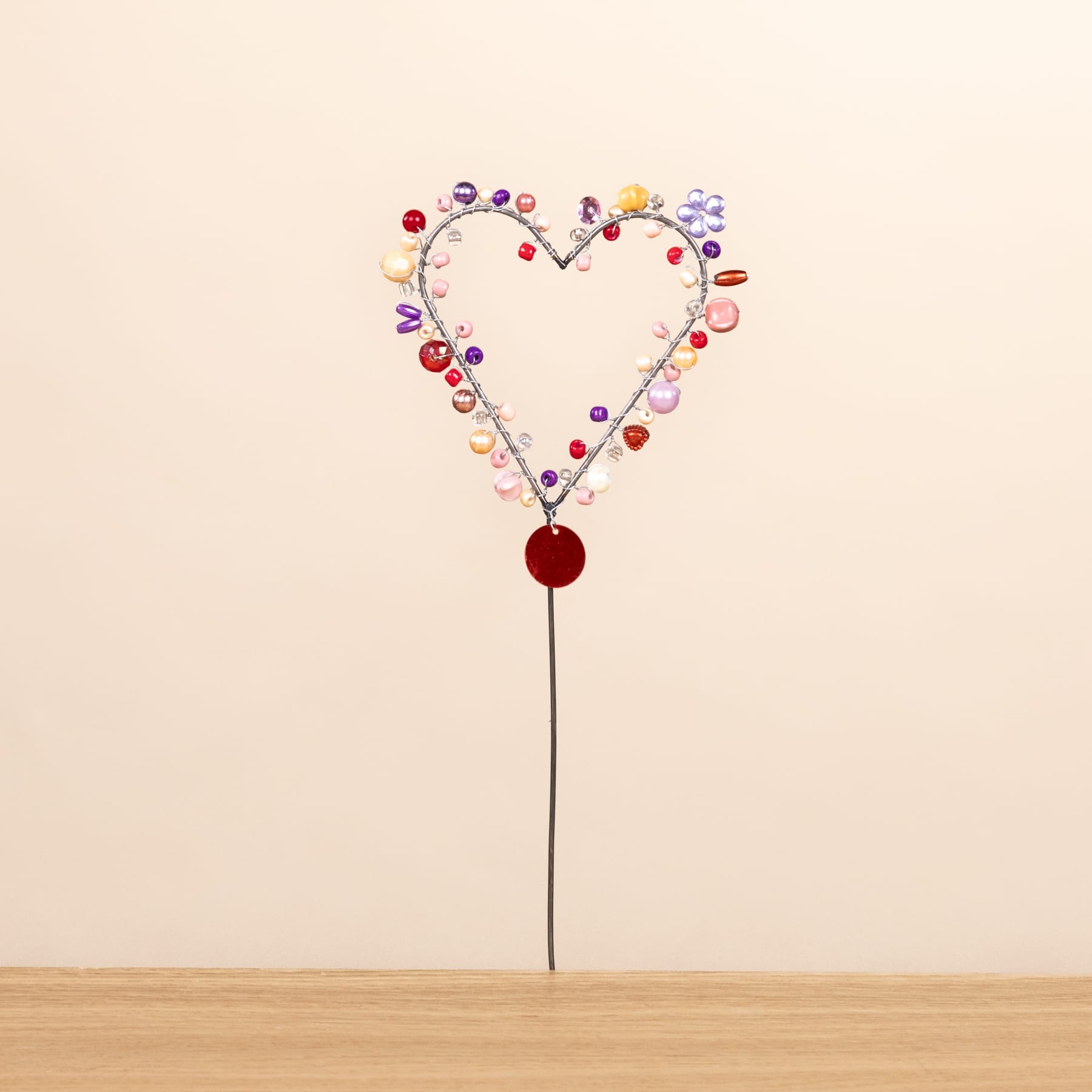 Eine herzförmige Anordnung bunter Knöpfe oder Perlen auf einer Holzoberfläche vor einem schlichten Hintergrund.