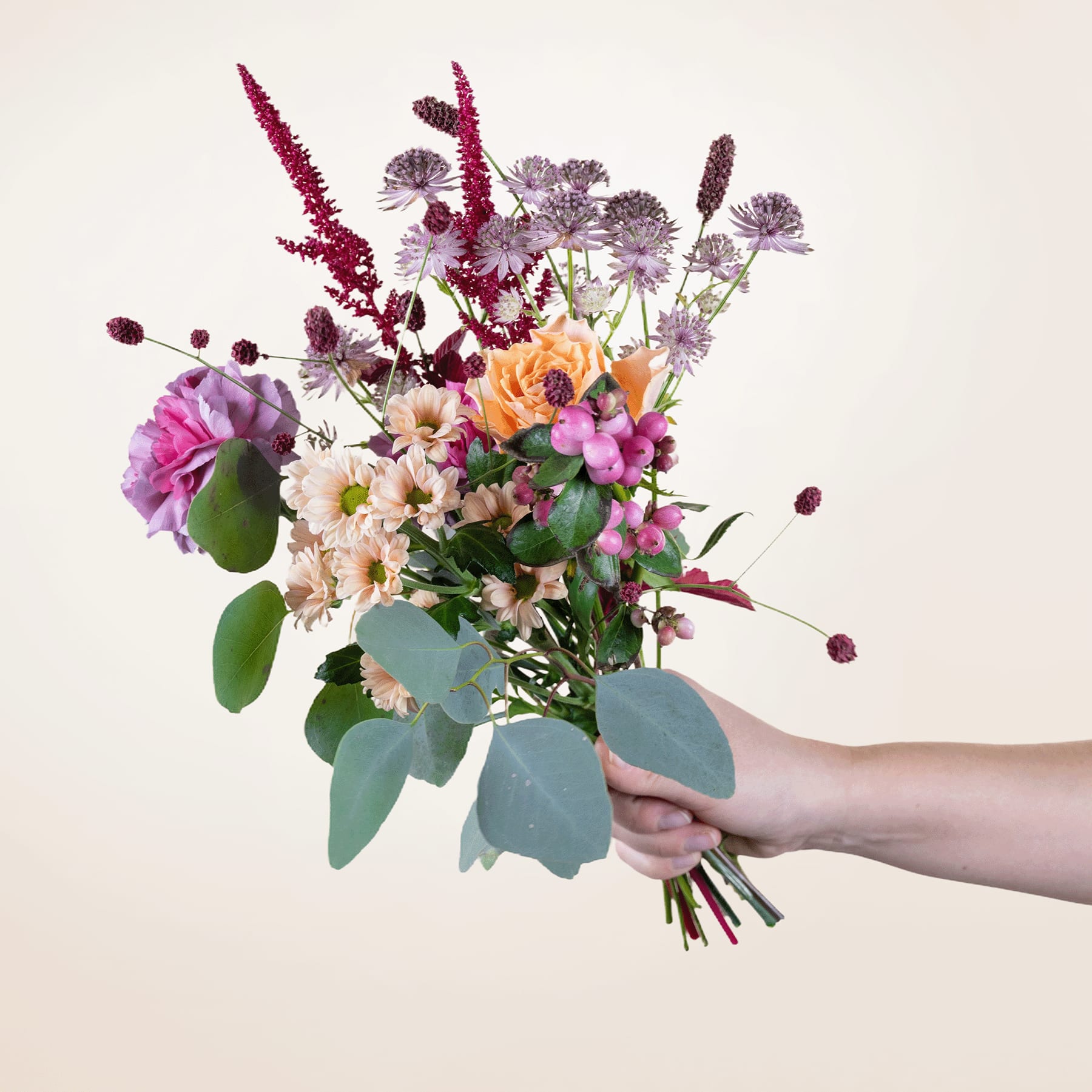 Ein leuchtender Strauß bunter Blumen, darunter rosa Pfingstrosen, orangefarbene Chrysanthemen und violette Strandflieder, wird vor einem schlichten Hintergrund in den Händen einer Person gehalten.