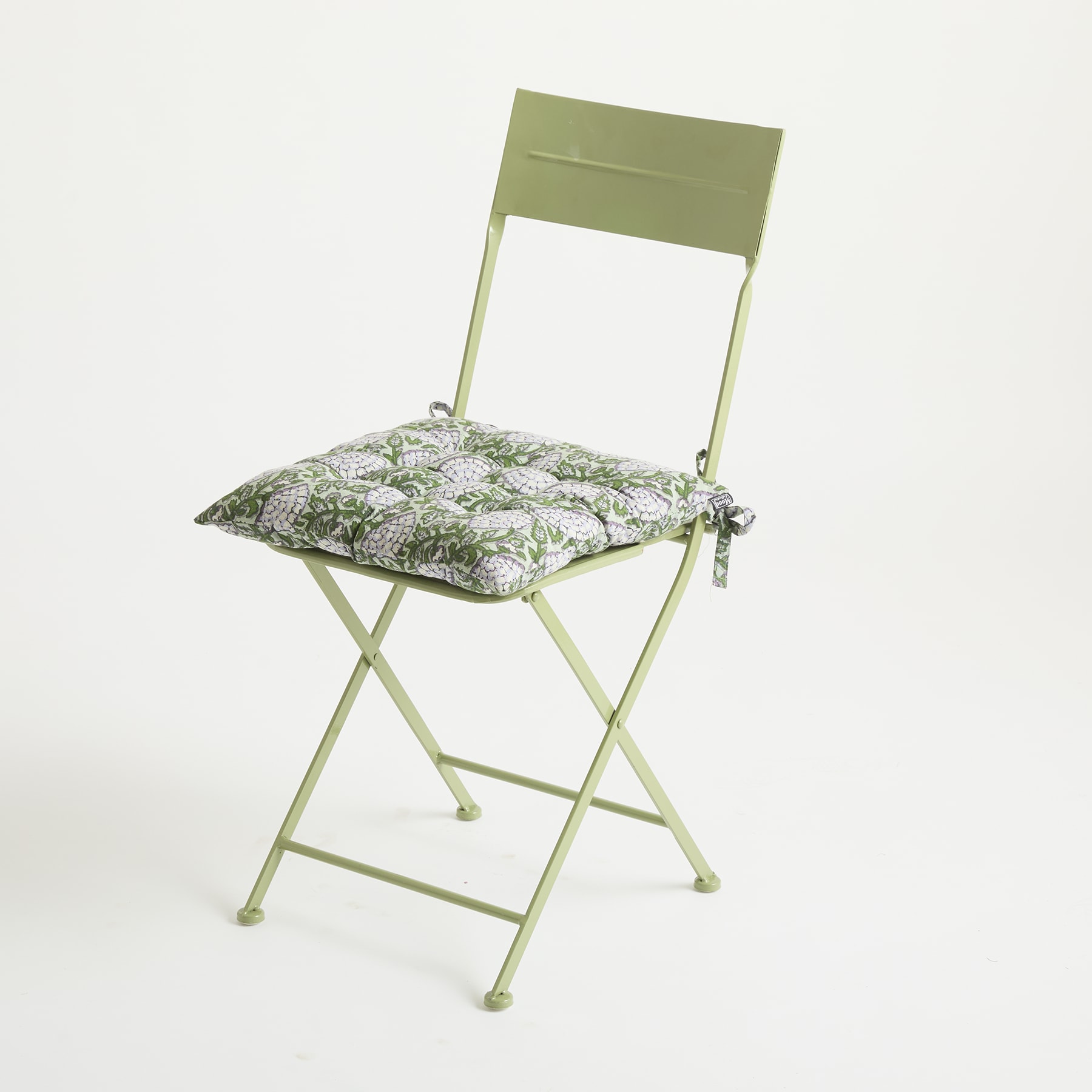Auf einem schlichten weißen Hintergrund steht ein grüner Klappstuhl aus Metall mit einem Kissen mit Blumenmuster.