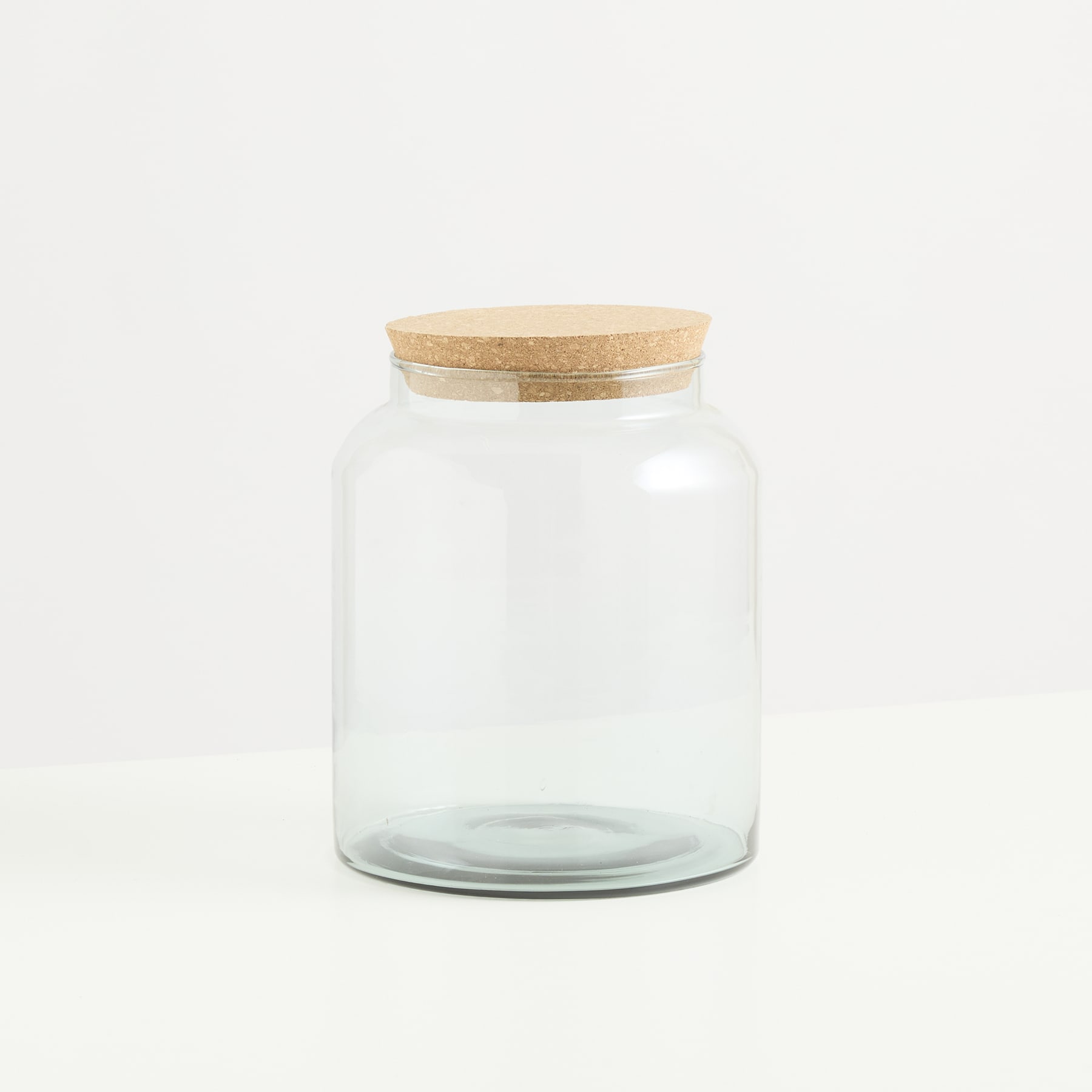 Auf einem schlichten weißen Hintergrund steht ein durchsichtiges Glasgefäß mit Holzdeckel.