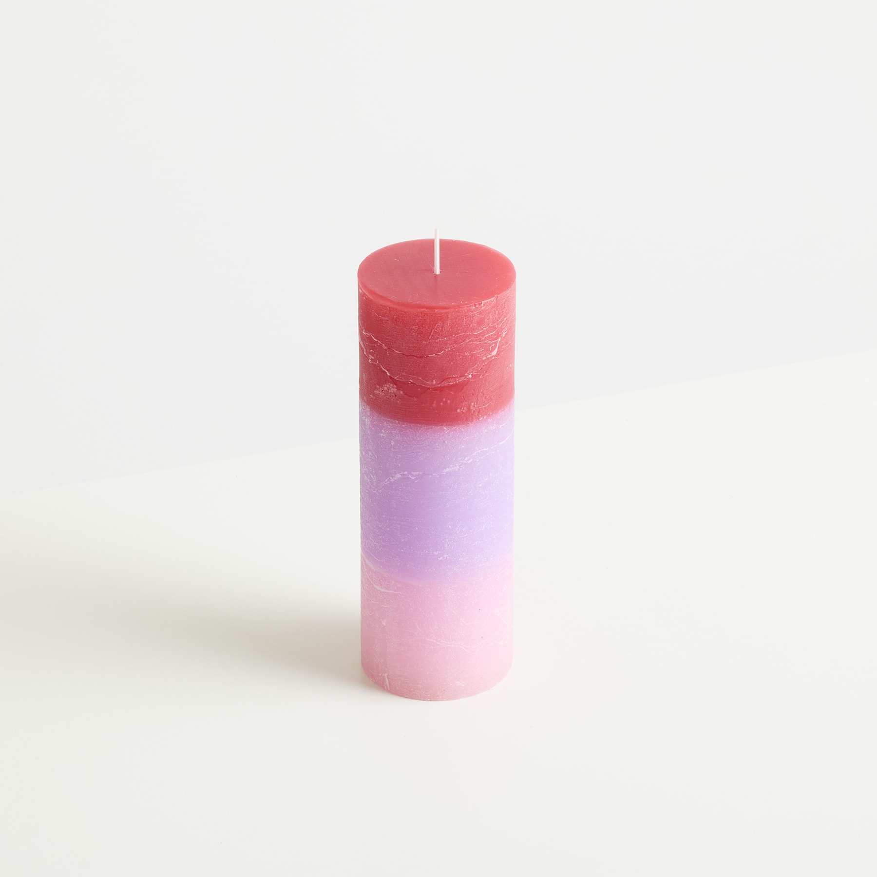 Eine zylindrische Kerze mit rotem Oberteil und einem rosa-weißen Farbverlaufsmuster auf dem Körper, vor einem schlichten weißen Hintergrund.