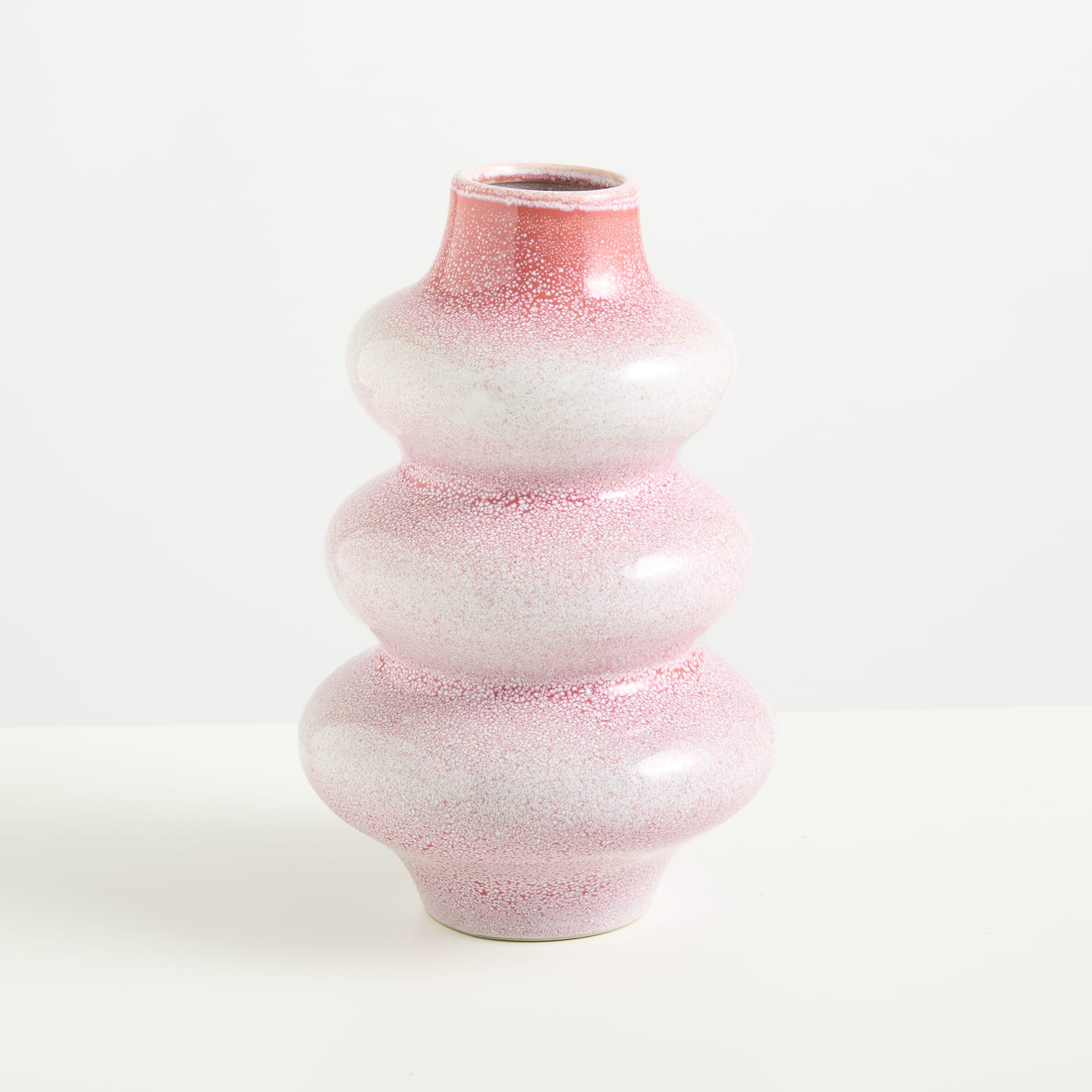 Eine rosa-weiße Keramikvase mit strukturiertem, geschichtetem Design steht vor einem schlichten weißen Hintergrund.