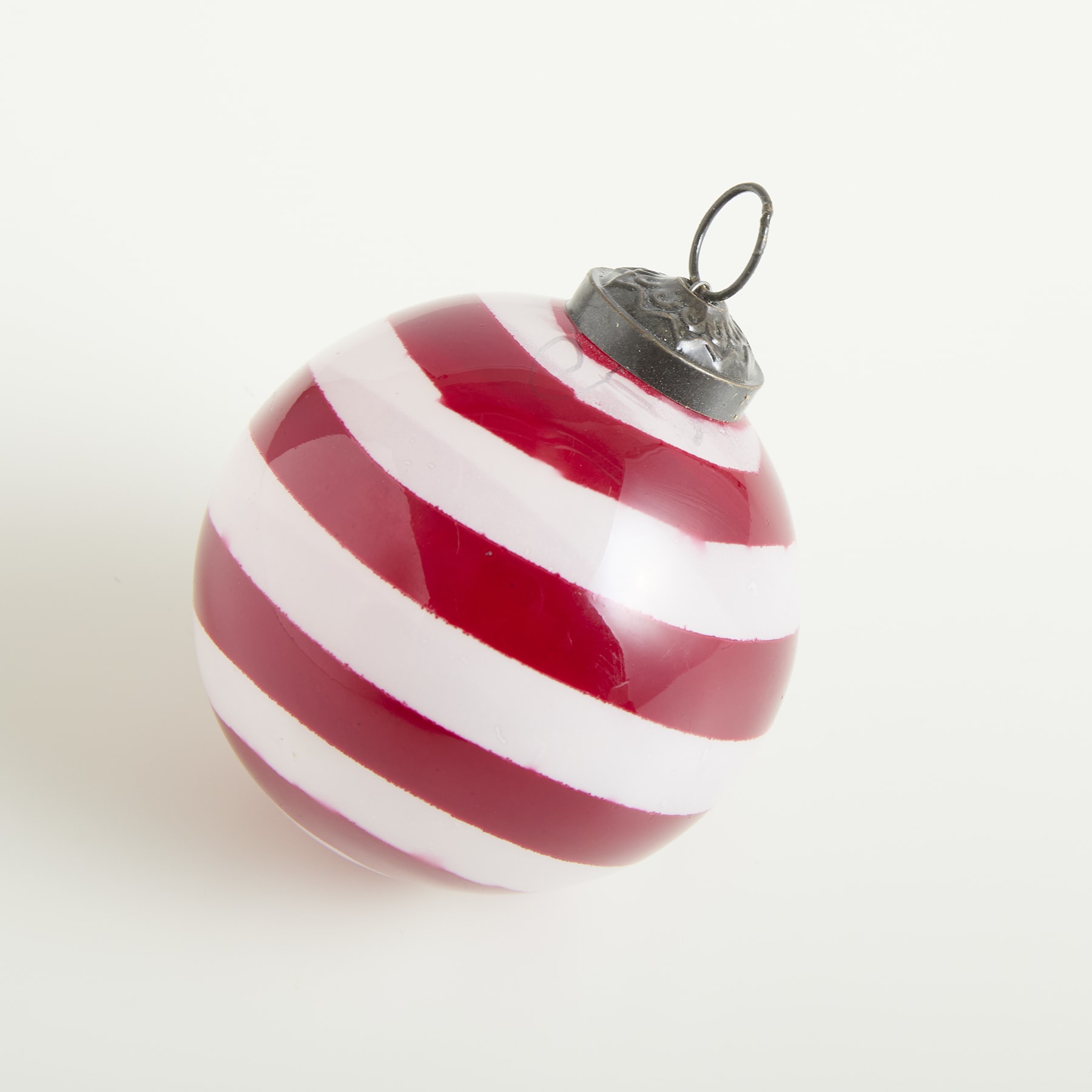 Ein rot-weiß gestreiftes Weihnachtsornament liegt auf einem schlichten weißen Hintergrund.