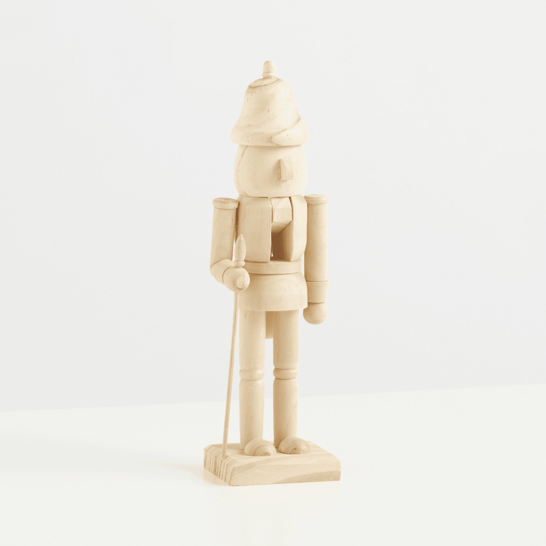 Eine hölzerne Nussknackerfigur steht allein auf einem schlichten weißen Hintergrund, wobei ihre komplizierten Details und geschnitzten Merkmale deutlich zur Geltung kommen.