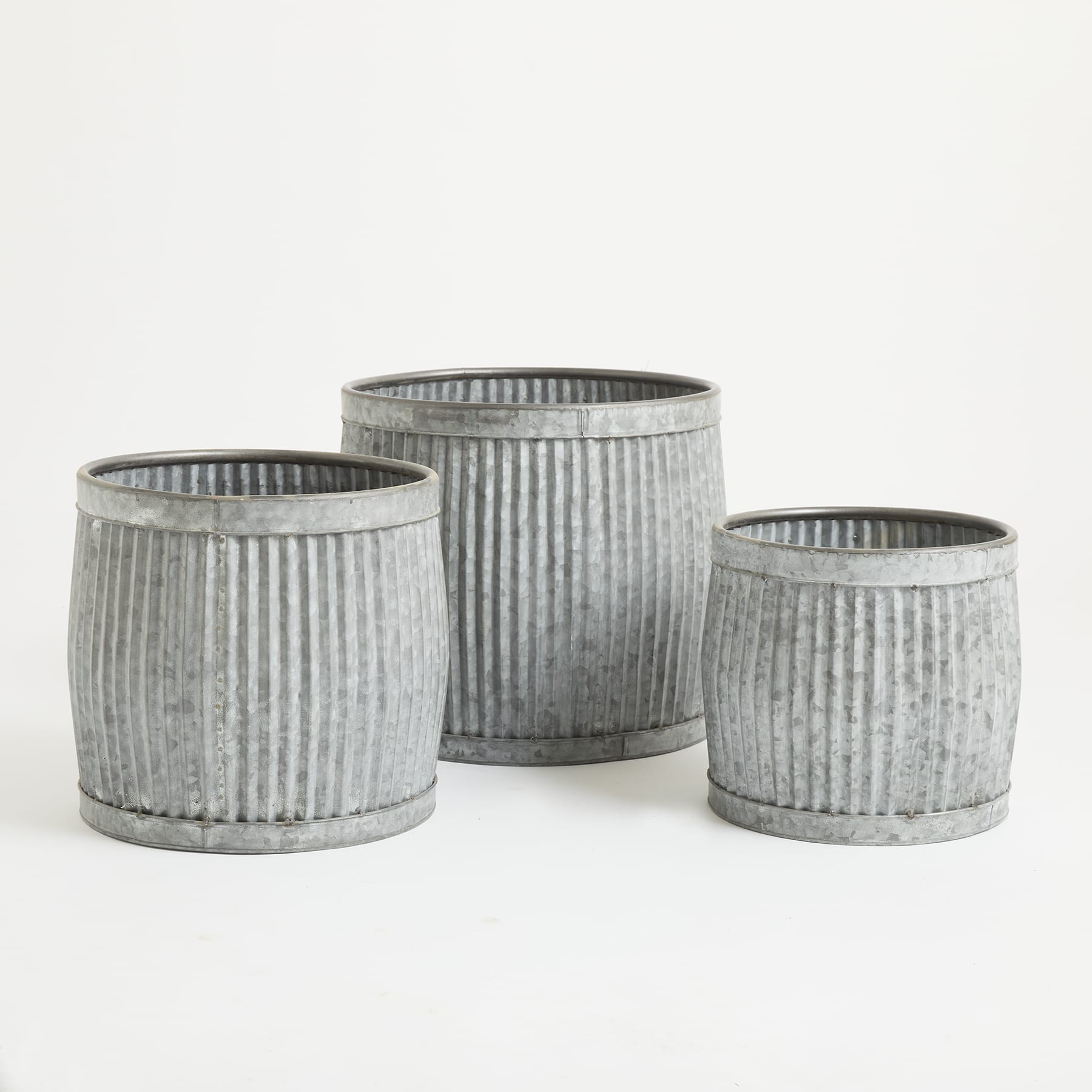 Drei Pflanzgefäße oder Behälter aus verzinktem Metall mit gerippter oder gewellter Struktur, in einer Gruppe auf einem schlichten weißen Hintergrund angeordnet.