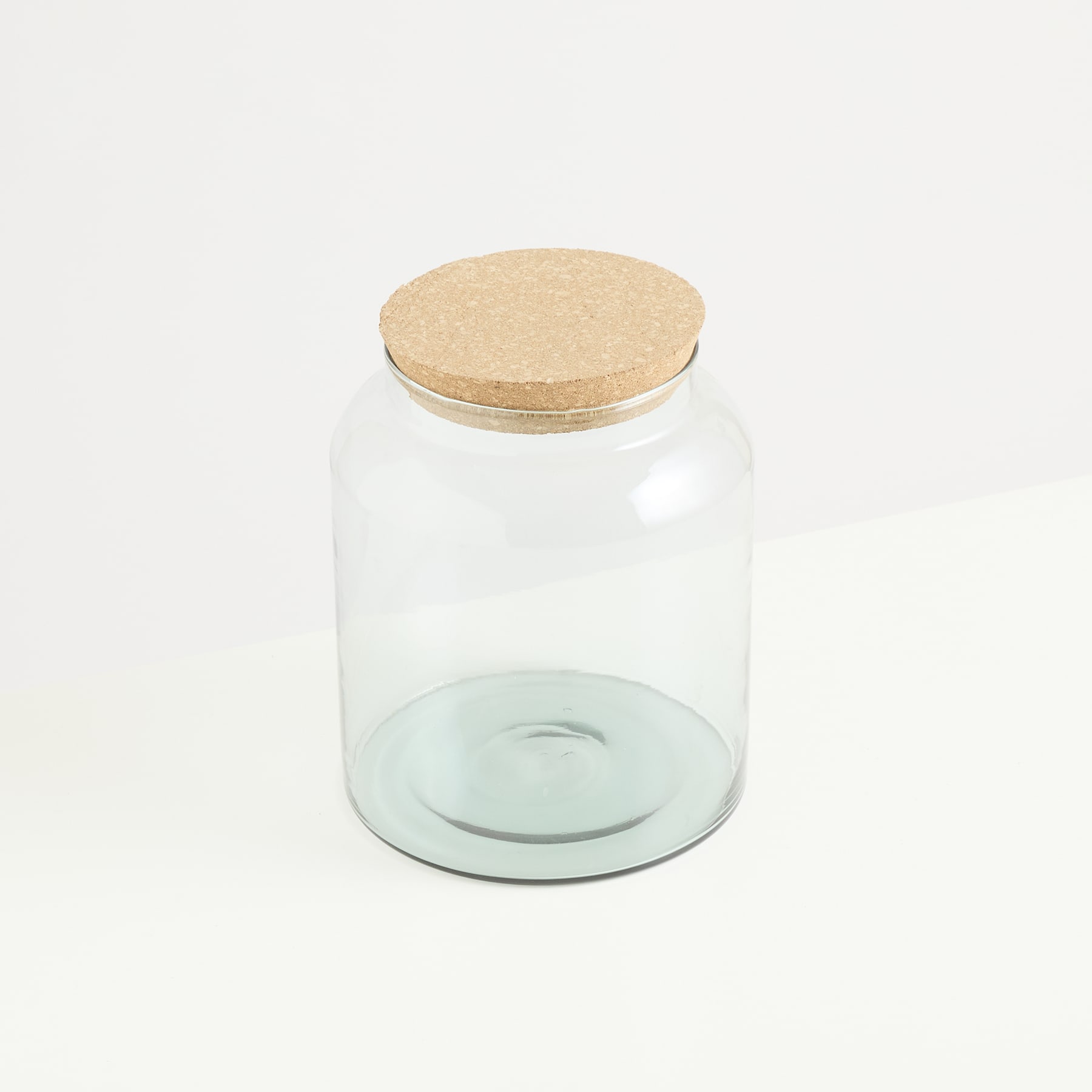 Auf einem schlichten weißen Hintergrund steht ein durchsichtiges Glasgefäß mit Holzdeckel.