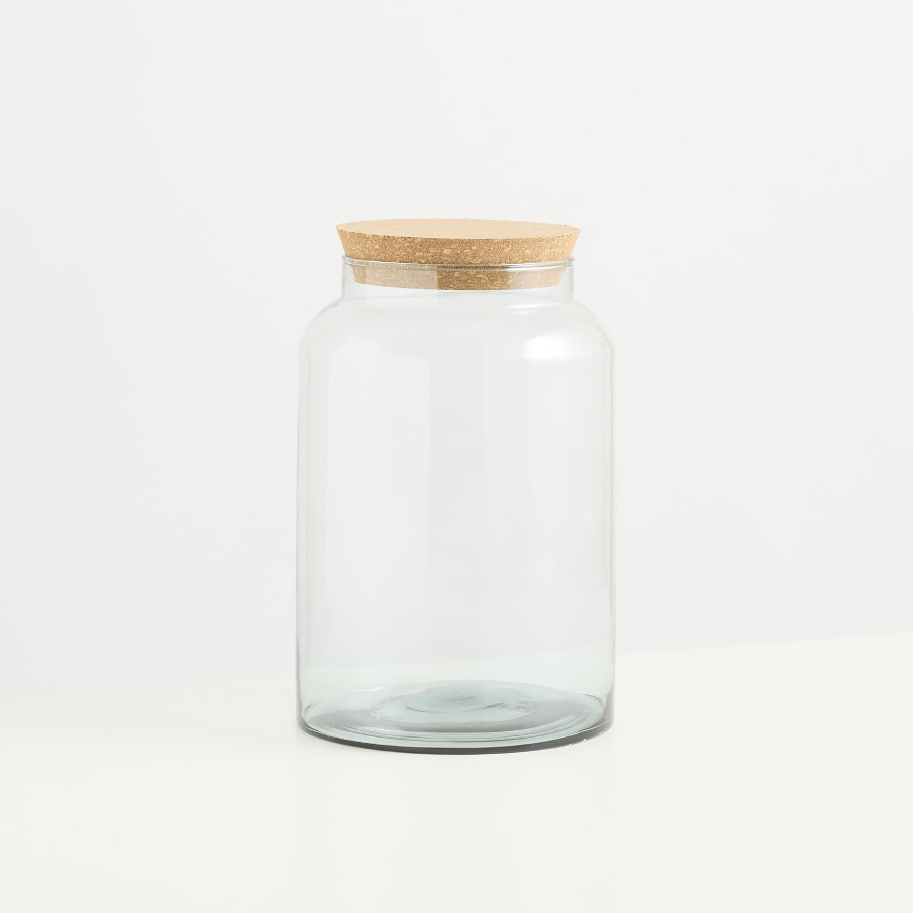 Auf einem schlichten weißen Hintergrund steht ein durchsichtiges Glasgefäß mit Holzdeckel.