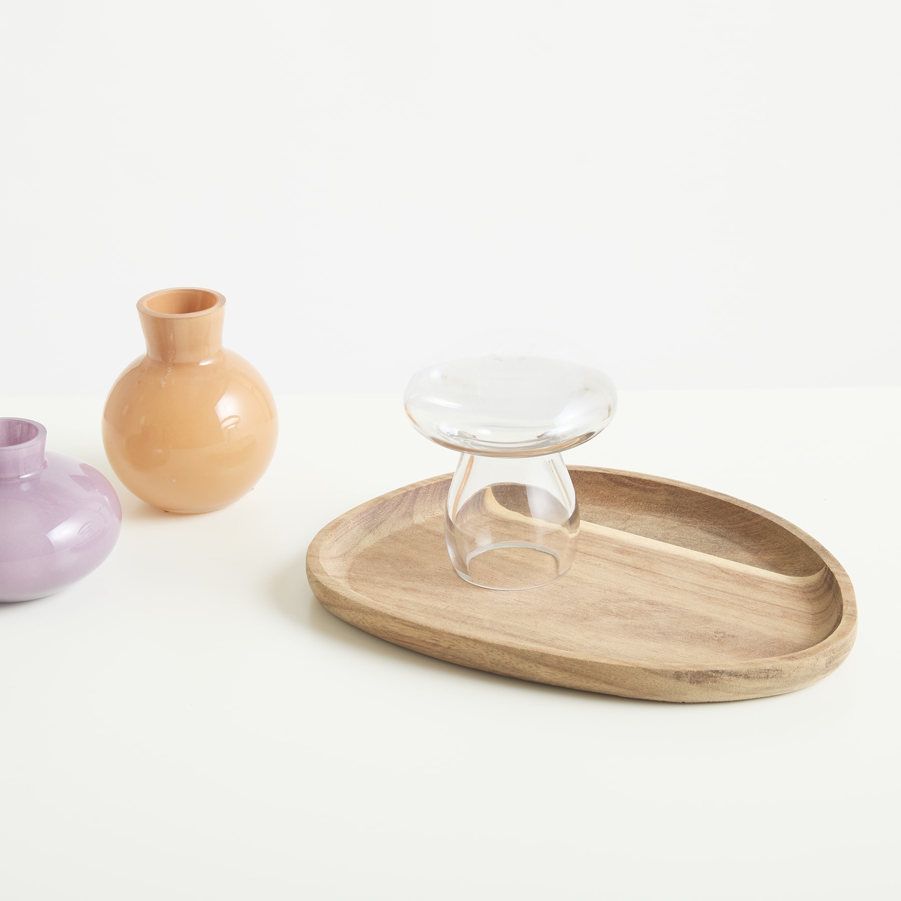 Ein Holztablett mit einem Glasbehälter und zwei Keramikvasen im Hintergrund, alles auf einer weißen Oberfläche platziert.