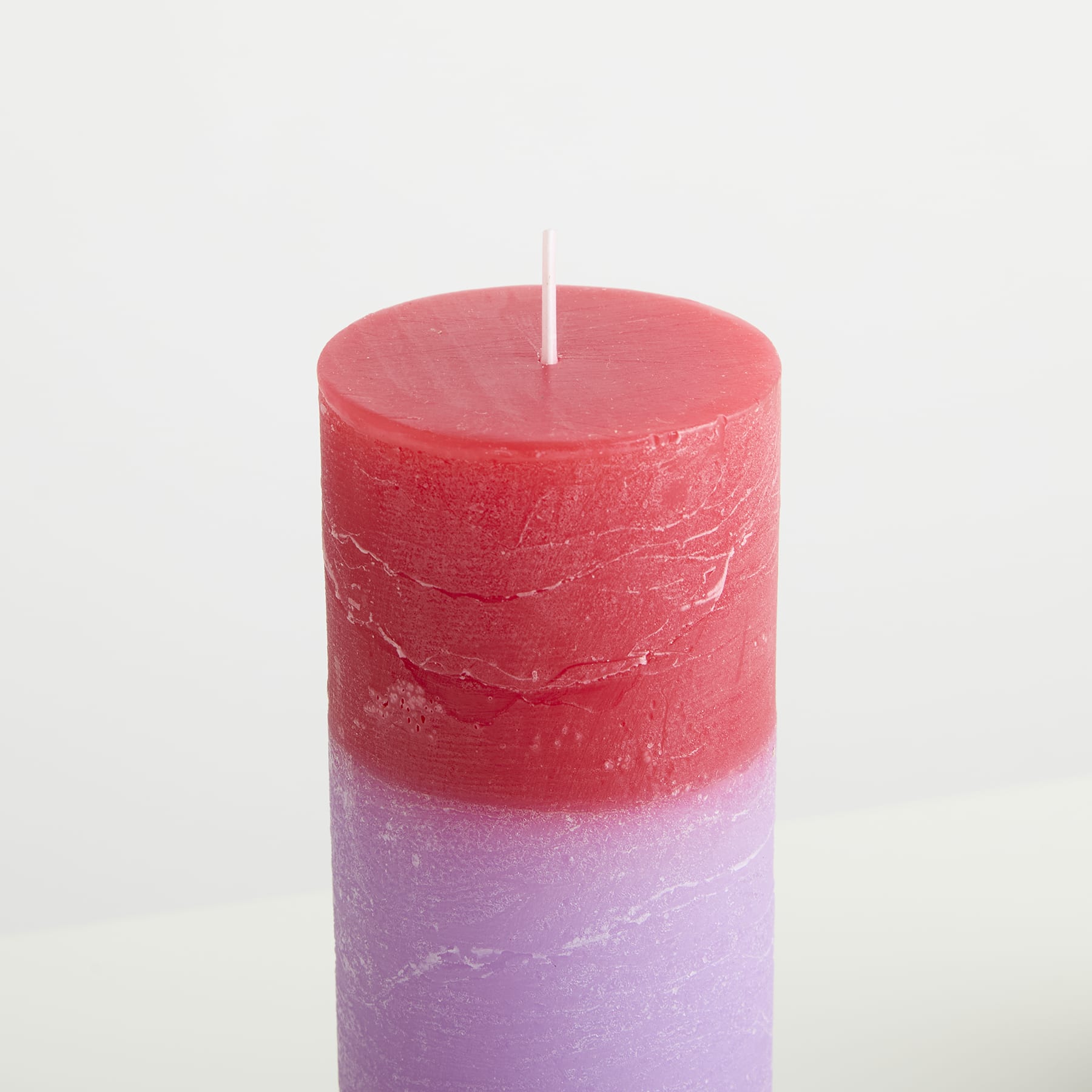 Eine rot-violette Kerze steht auf einem schlichten weißen Hintergrund.