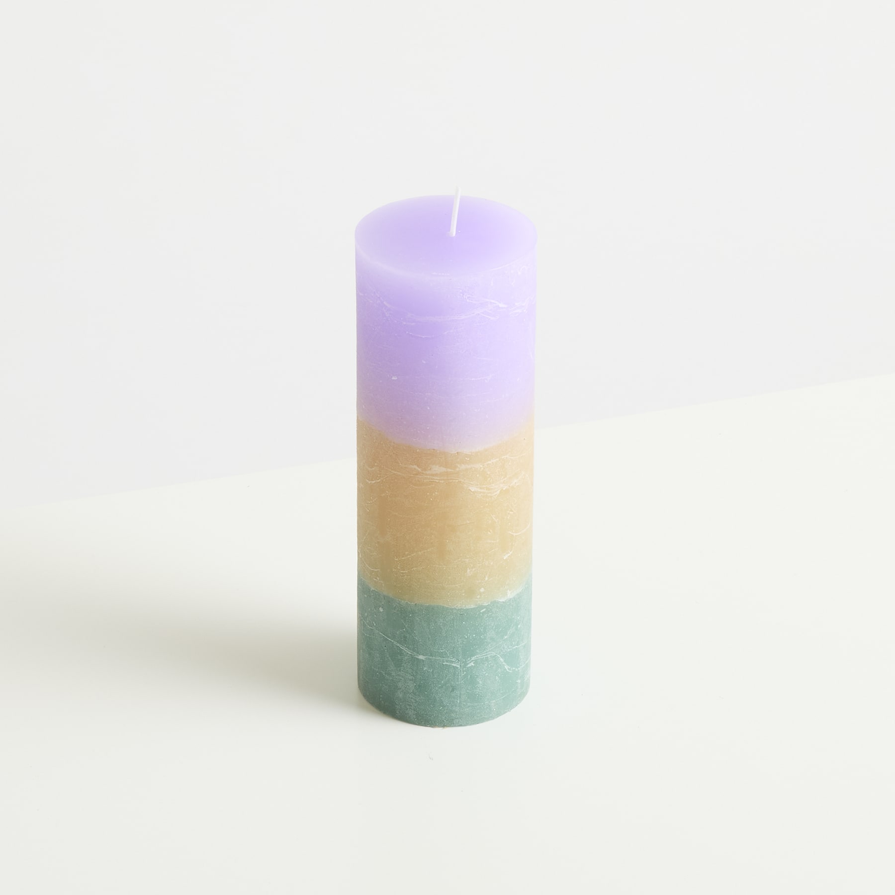 Eine pastellfarbene Kerze mit Schichten aus Lavendel, Beige und Mintgrün steht aufrecht auf einem schlichten Hintergrund.