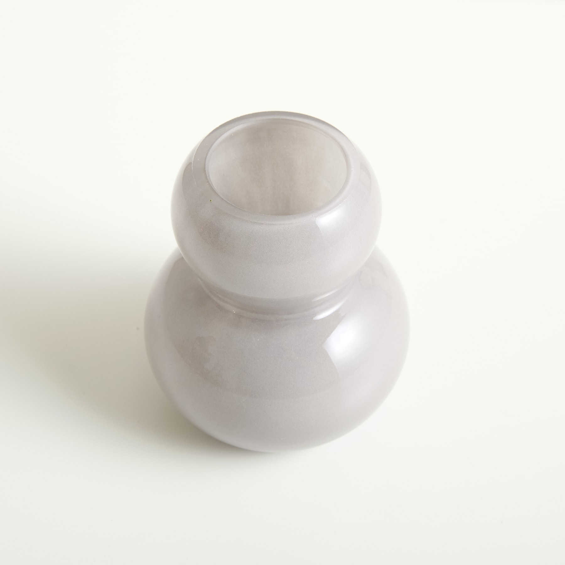 Eine weiße, kugelförmige Vase oder ein Gefäß aus Keramik steht auf einer schlichten, hellen Oberfläche und wirft einen weichen, diffusen Schatten.