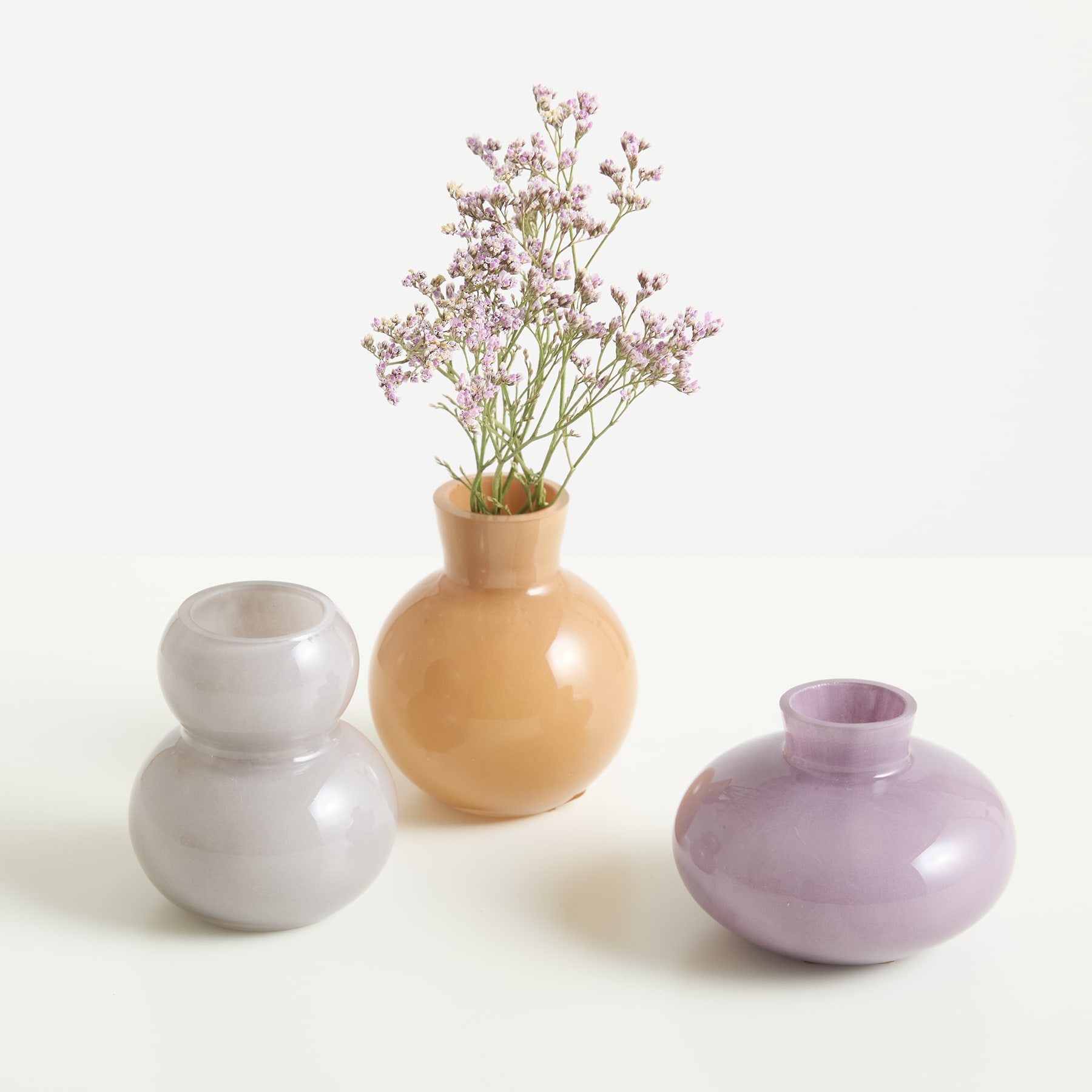 Das Bild zeigt eine Vase mit zarten rosa Blumen neben zwei weiteren Keramikvasen in ergänzenden Pastellfarben, alle vor einem schlichten weißen Hintergrund.