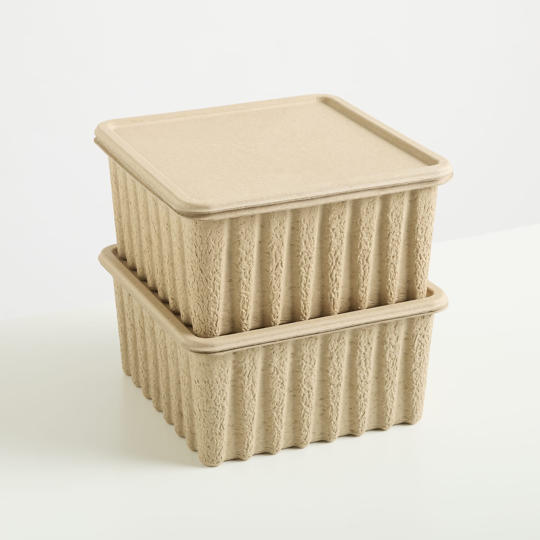 Zwei quadratische beige Behälter mit strukturierten Oberflächen und Deckeln stehen auf einem schlichten weißen Hintergrund.
