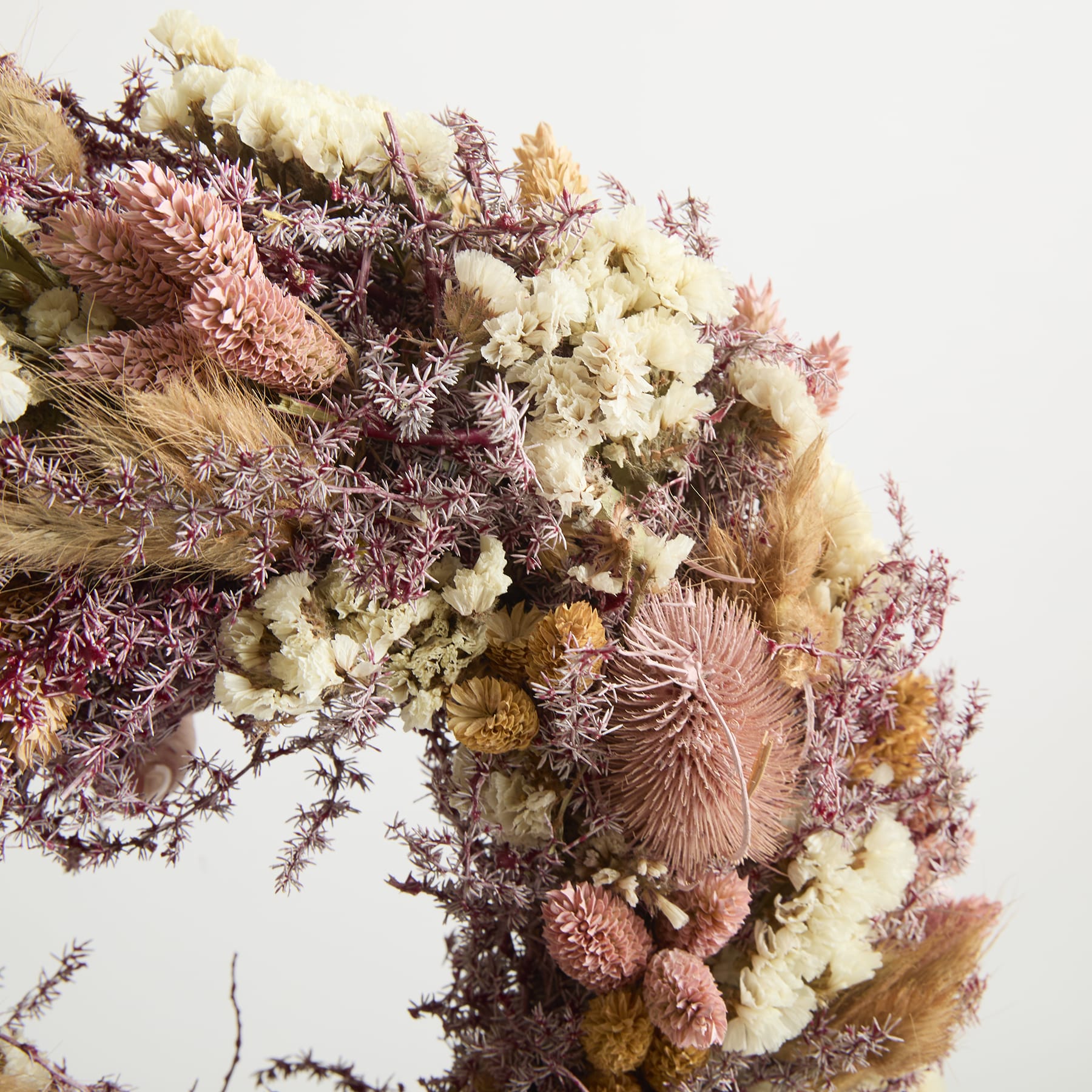 Ein lebendiger Strauß getrockneter Blumen in Rosa-, Gelb- und Weißtönen, arrangiert in einer optisch auffälligen und strukturierten Komposition vor einem schlichten Hintergrund.