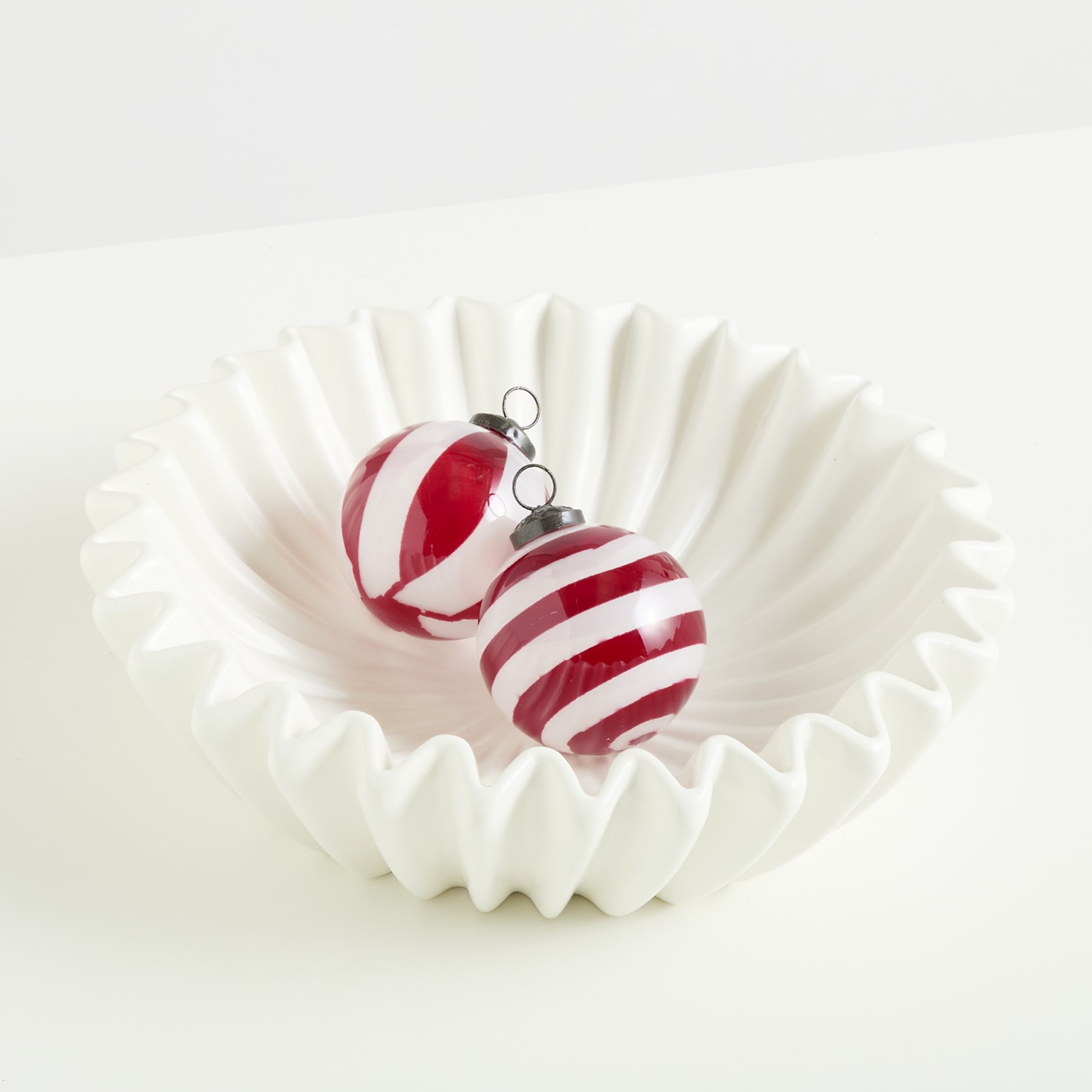Das Bild zeigt ein rot-weiß gestreiftes Weihnachtsornament in einer weißen Cupcake-Förmchen vor einem schlichten weißen Hintergrund.