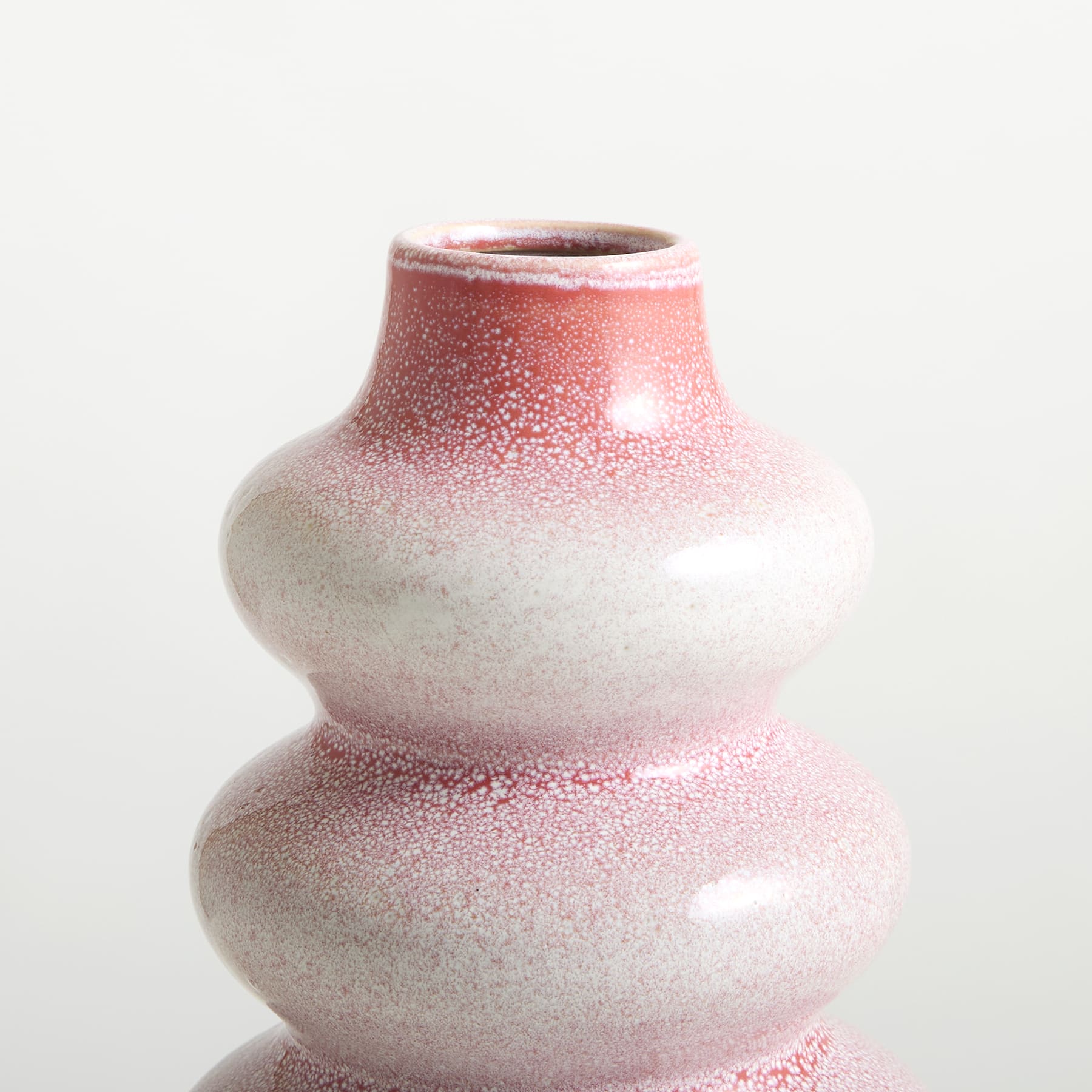 Eine rosa-weiße Keramikvase mit strukturierter, gesprenkelter Oberfläche steht vor einem schlichten weißen Hintergrund.