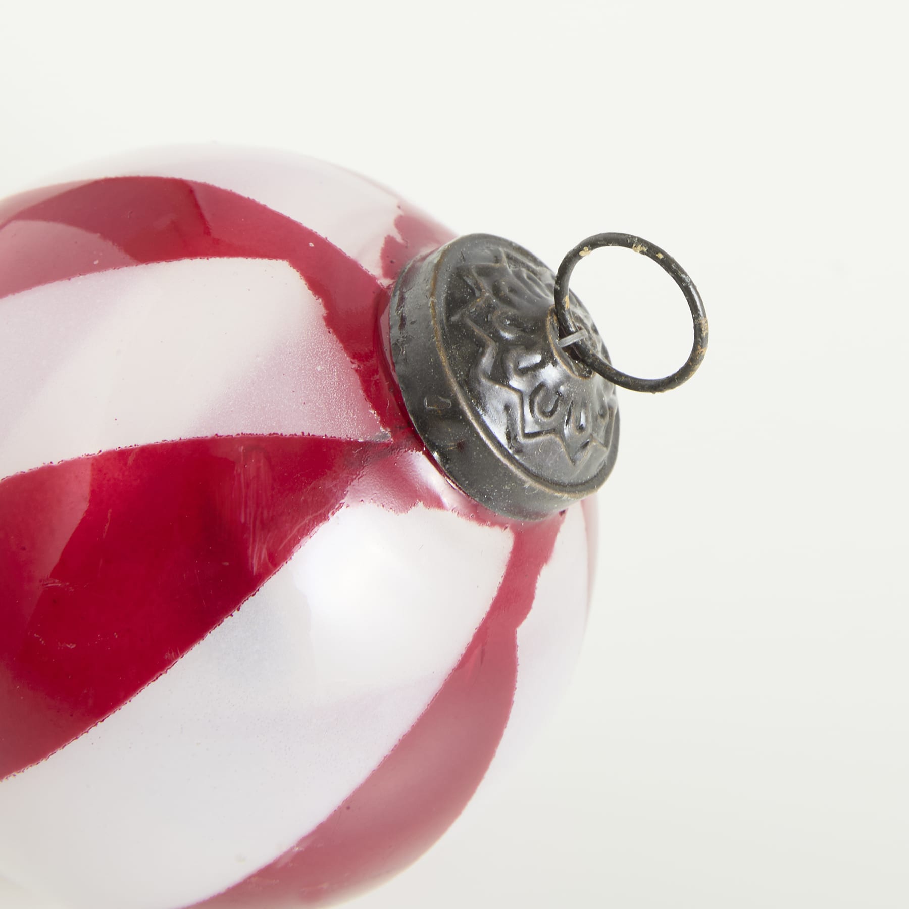Ein rot-weiß gestreiftes Ornament mit einem metallischen Dekorationselement in der Mitte vor einem schlichten weißen Hintergrund.