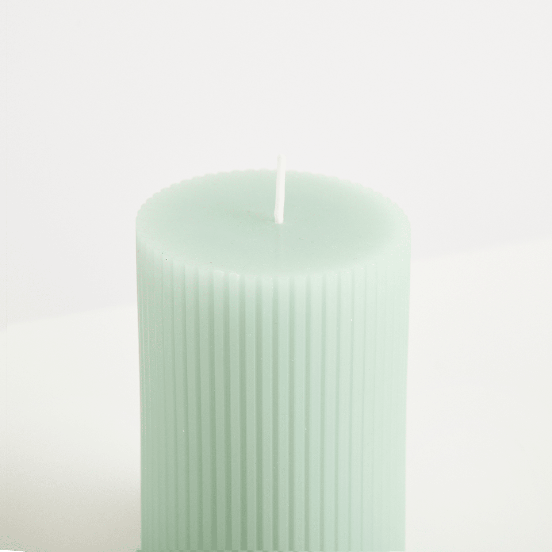 Eine mintfarbene, vertikal gerippte Kerze steht vor einem schlichten weißen Hintergrund.
