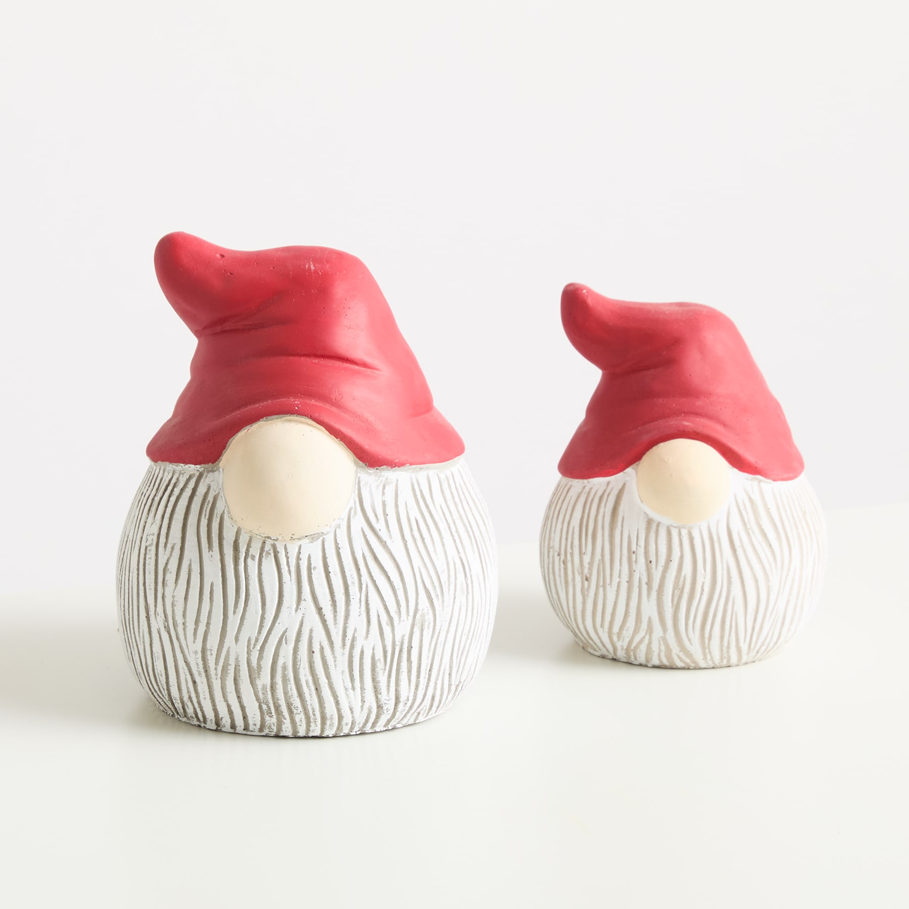 Zwei skurrile Keramikzwerge mit weißen Körpern und roten Hüten sitzen auf einem schlichten weißen Hintergrund.