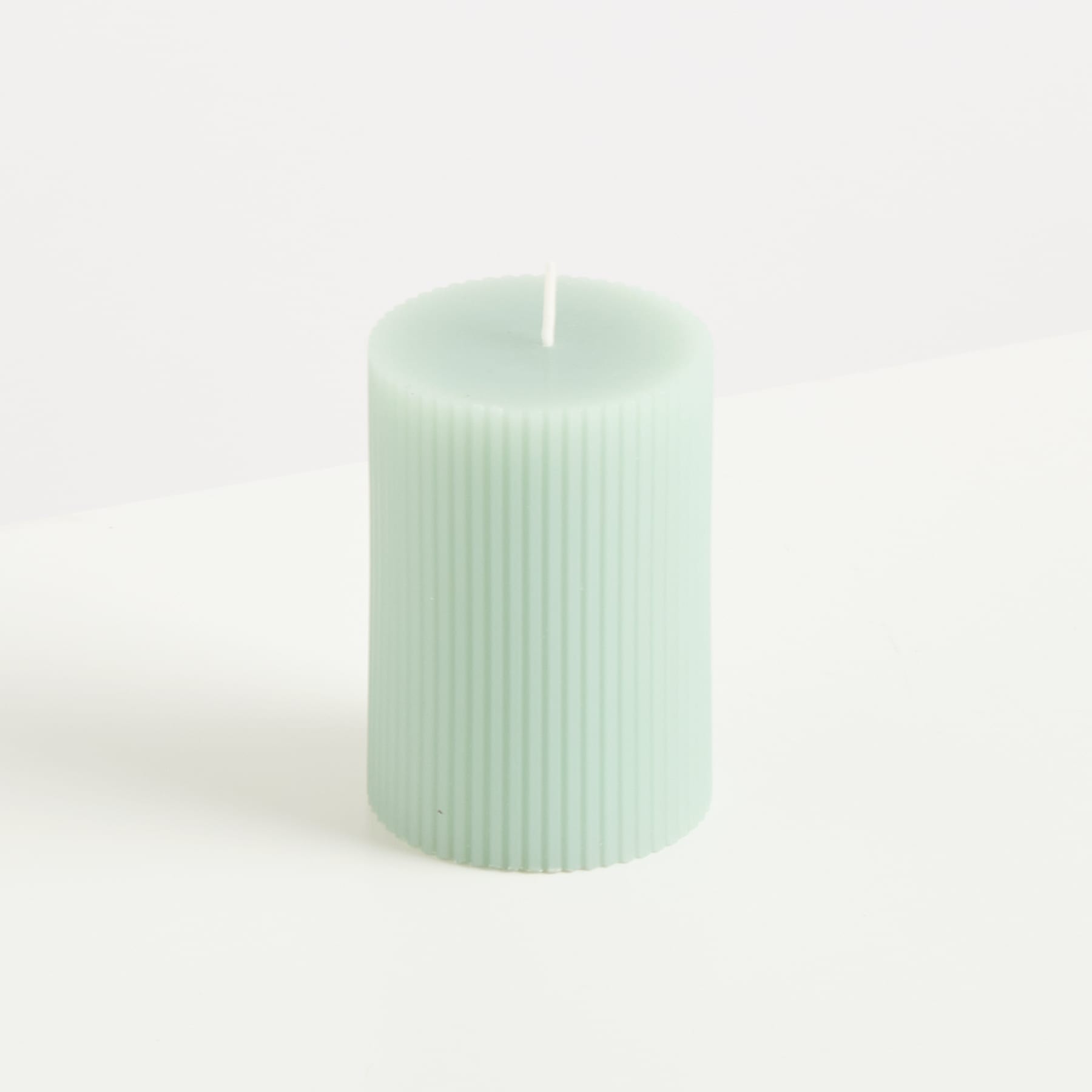 Eine mintfarbene, zylindrische Kerze mit vertikalen Rillen steht vor einem schlichten, weißen Hintergrund.