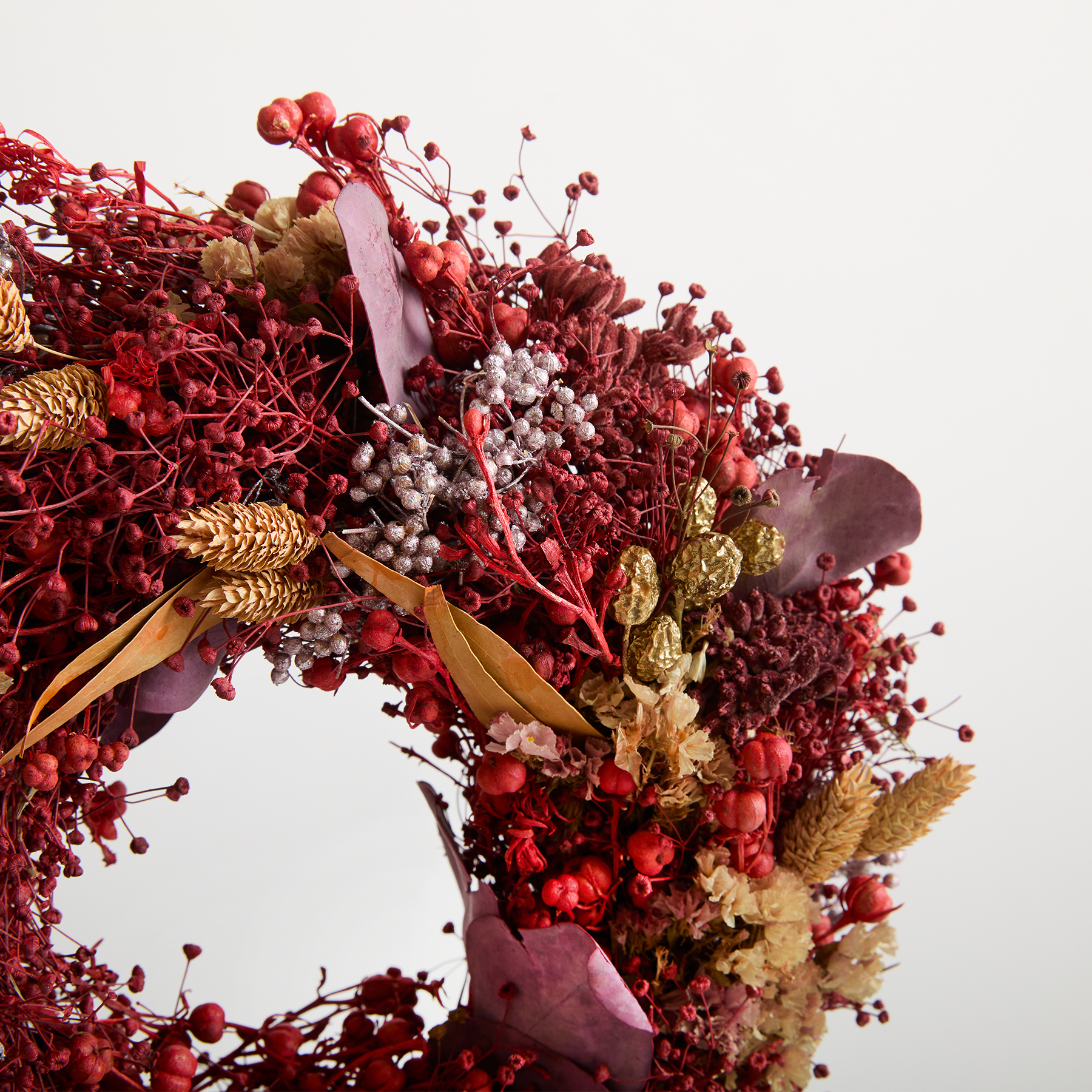 Ein lebendiges und üppiges Blumenarrangement aus verschiedenen Rottönen, darunter Beeren, Blumen und Blätter, vor einem schlichten weißen Hintergrund.