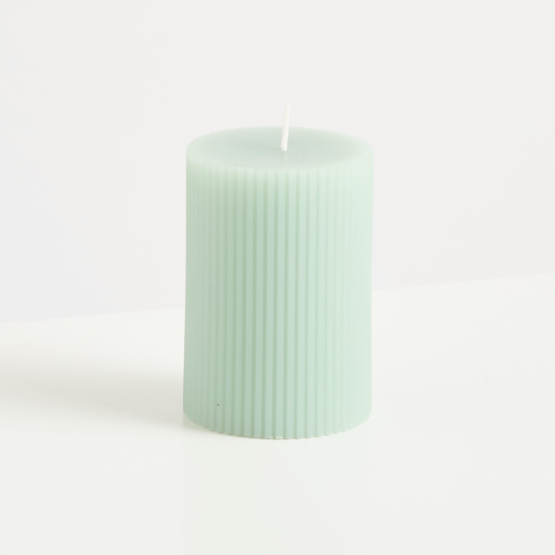 Eine mintfarbene, zylindrische Kerze mit vertikalen Rillen steht vor einem schlichten weißen Hintergrund.