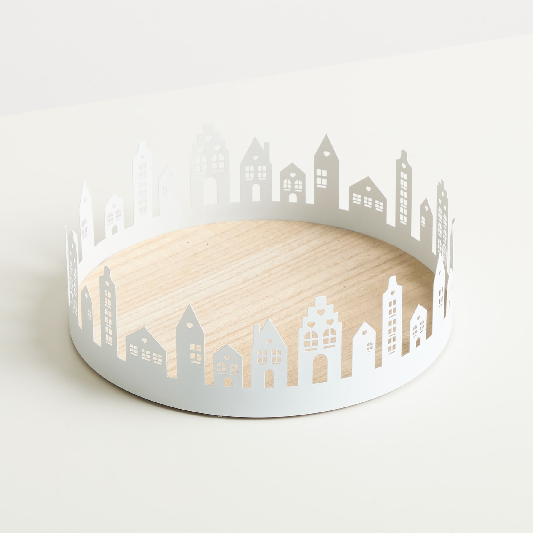 Ein rundes Holztablett mit der weißen Silhouette einer Stadtlandschaft am Rand, das auf einer hellen Oberfläche ruht.