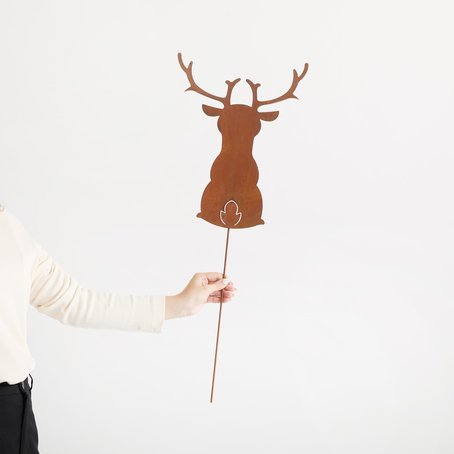 Eine Hand hält einen Holzausschnitt eines Hirsches mit Geweih vor einem schlichten weißen Hintergrund.