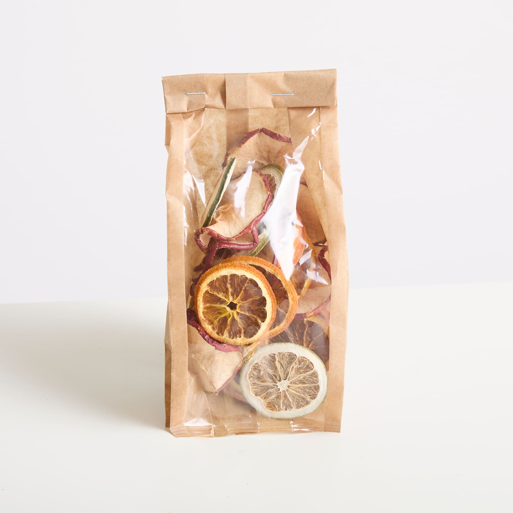Eine Papiertüte mit getrockneten Zitrusscheiben, darunter Zitrone und Orange, angeordnet auf einem schlichten Hintergrund.