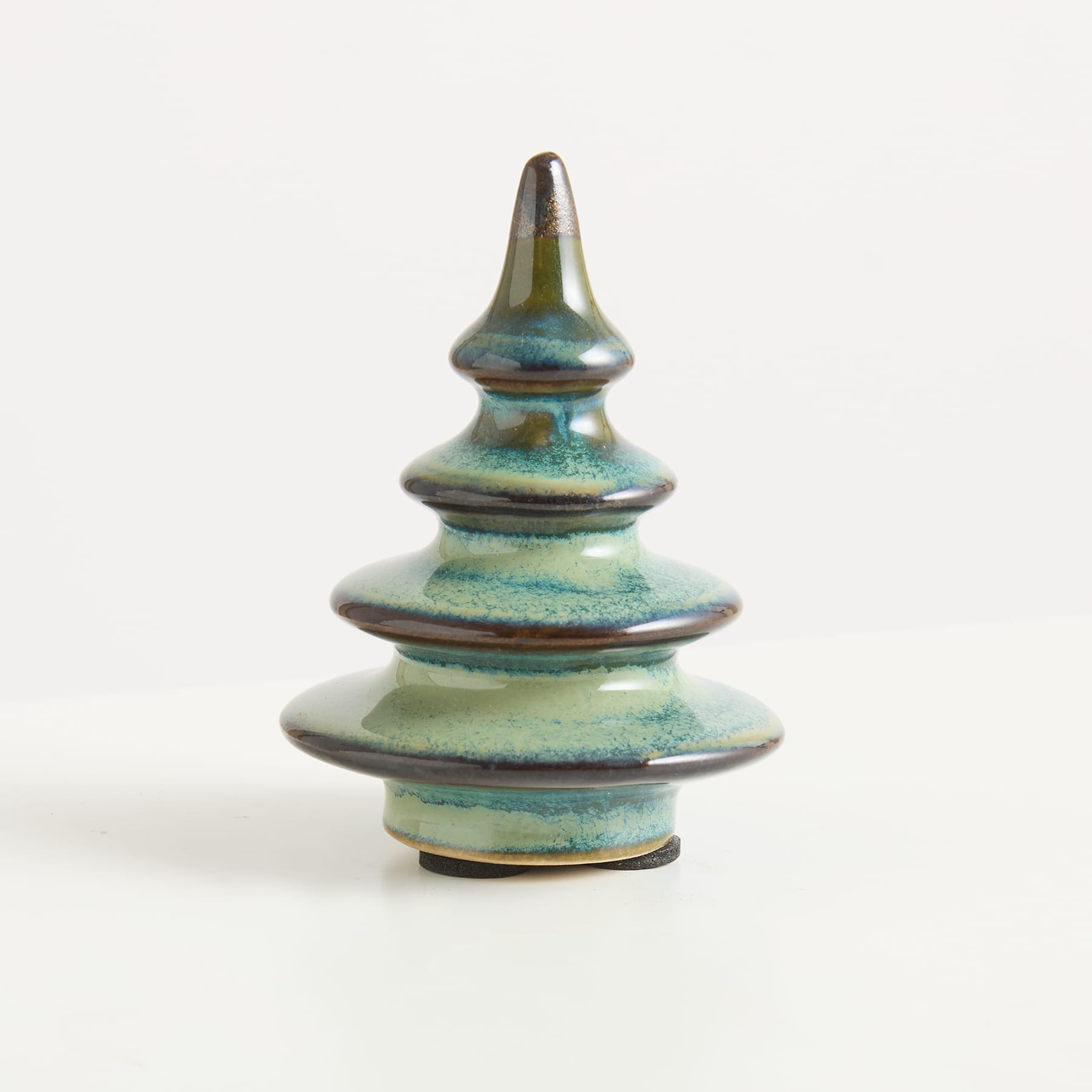 Ein Keramikornament in Form eines stilisierten Weihnachtsbaums mit grüner und blauer Glasur steht vor einem schlichten weißen Hintergrund.