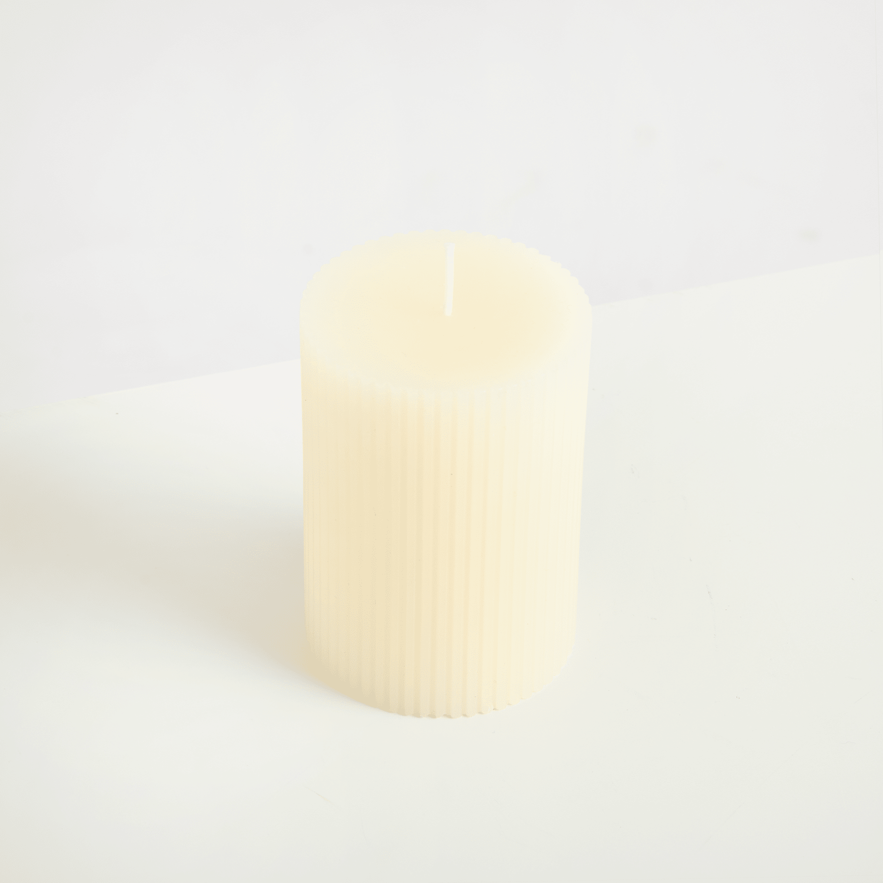 Eine einfache, cremefarbene Kerze steht allein auf einem schlichten, weißen Hintergrund.